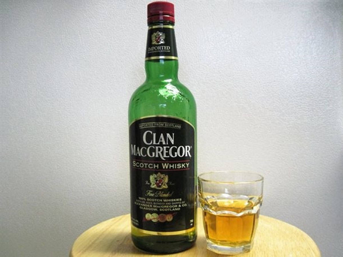 Whiskey 桌布 壁紙 — 一瓶綠色的Clan MacGregor蘇格蘭威士忌站在一個裝有琥珀色液體的玻璃杯旁邊，放在一張木桌上，背景是一面素色牆。