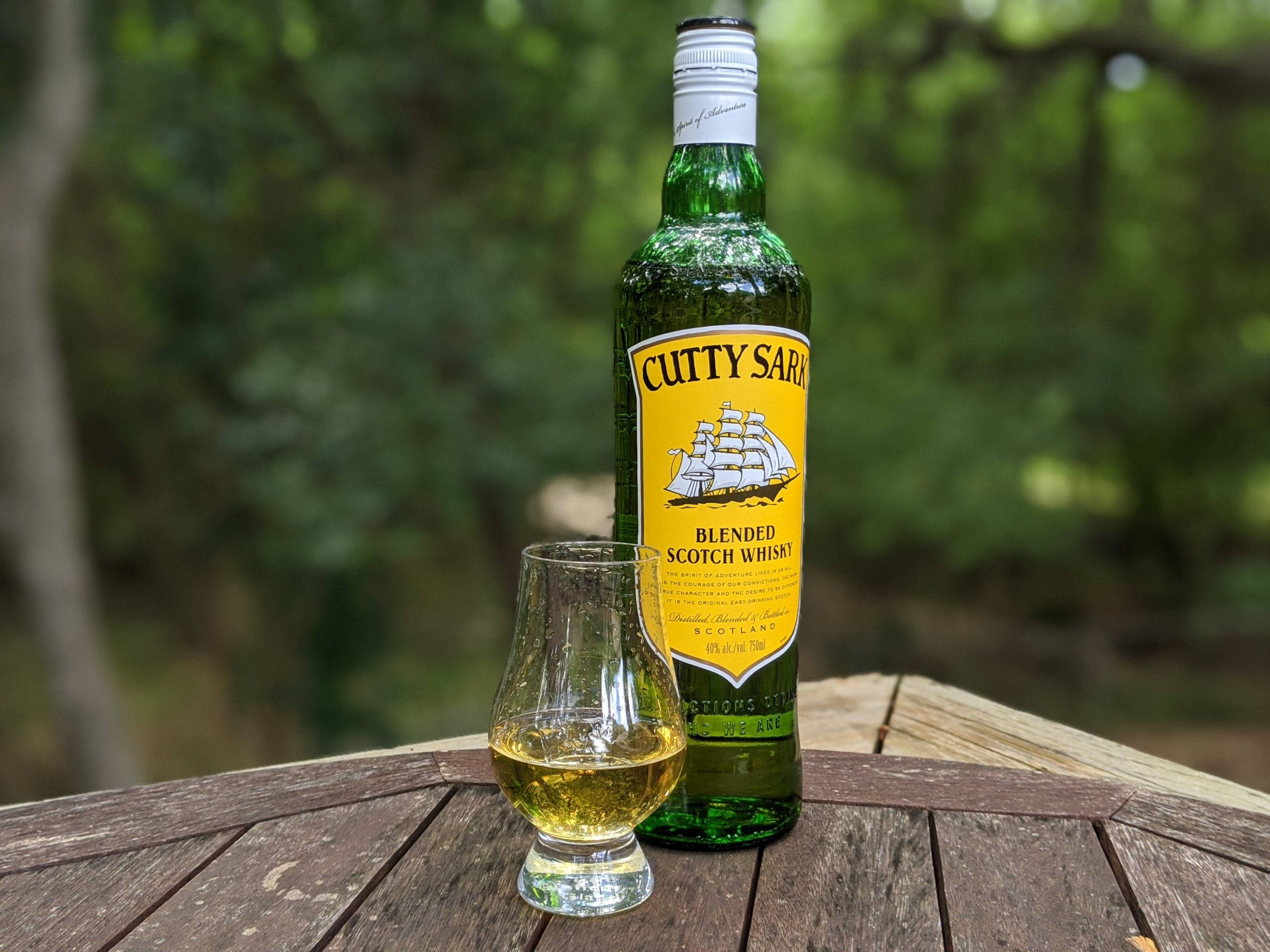 alcohol 桌布 壁紙 — 一瓶綠色的Cutty Sark調和蘇格蘭威士忌和一個裝滿酒的杯子，放在戶外一張風化的木桌上。