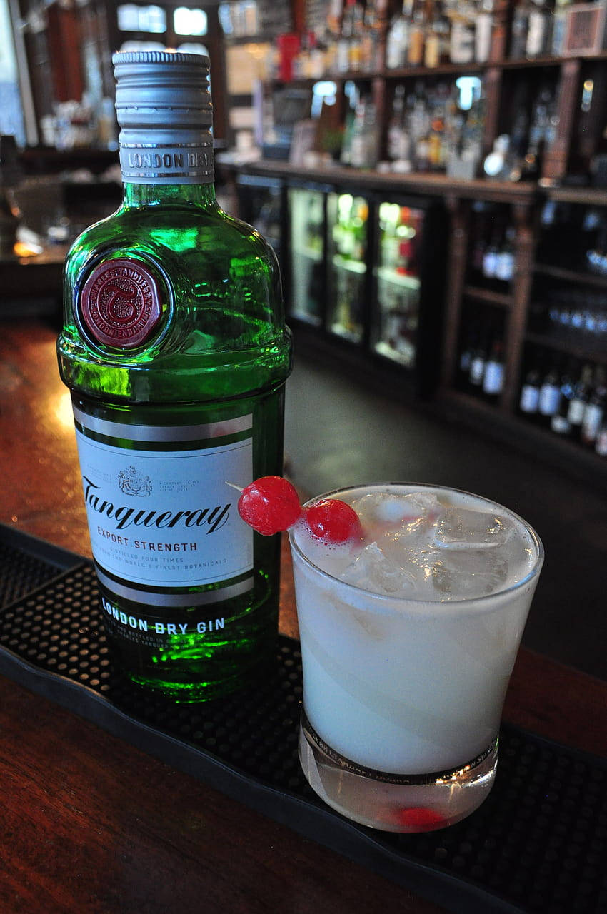 alcohol 桌布 壁紙 — 一瓶綠色的Tanqueray琴酒放在吧檯墊上，旁邊是一杯用櫻桃裝飾的冰凍雞尾酒。
