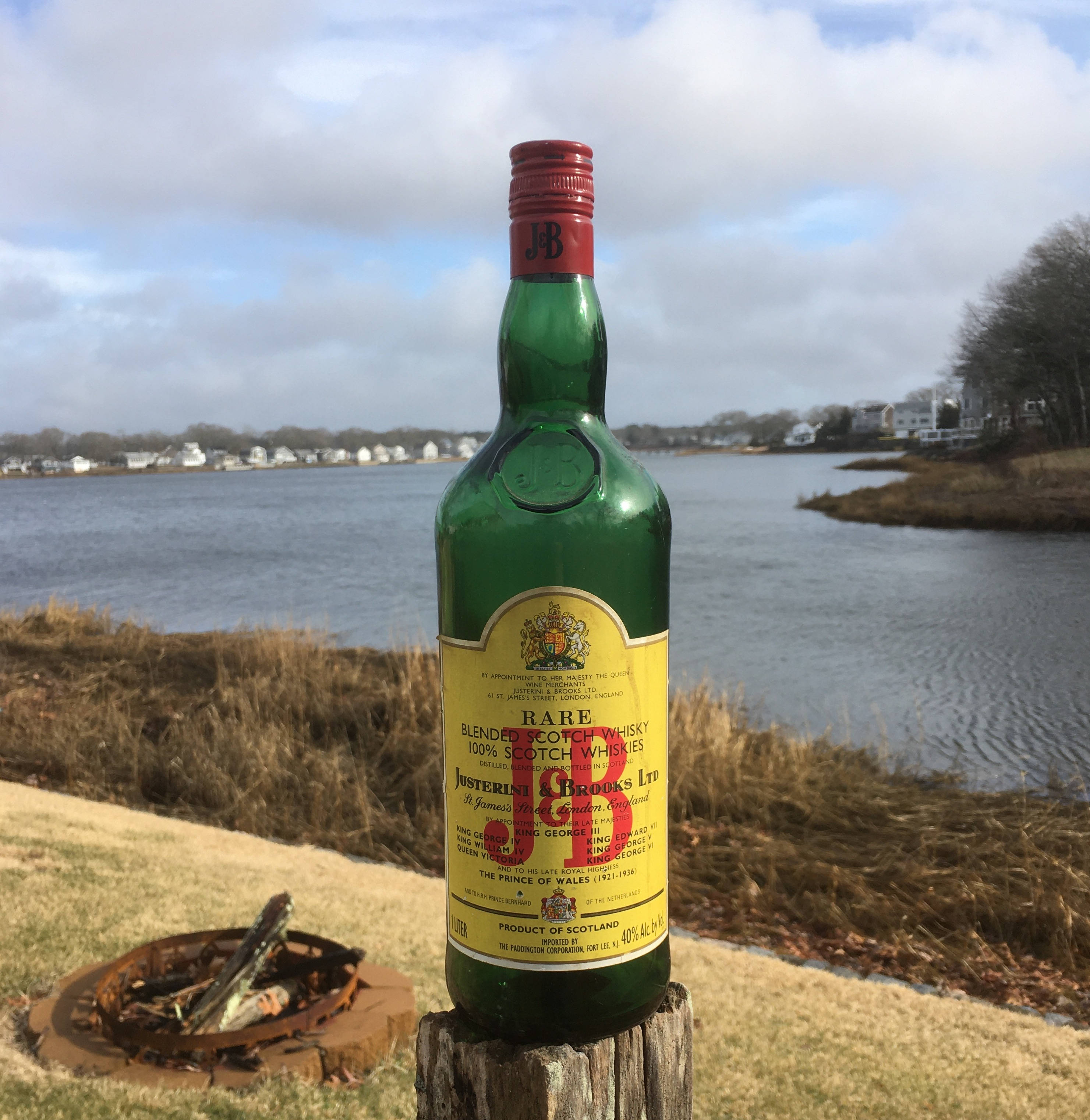 drinks 桌布 壁紙 — 一瓶罕見的蘇格蘭威士忌綠色瓶子，立在多雲天空下平靜水邊的木樁上。