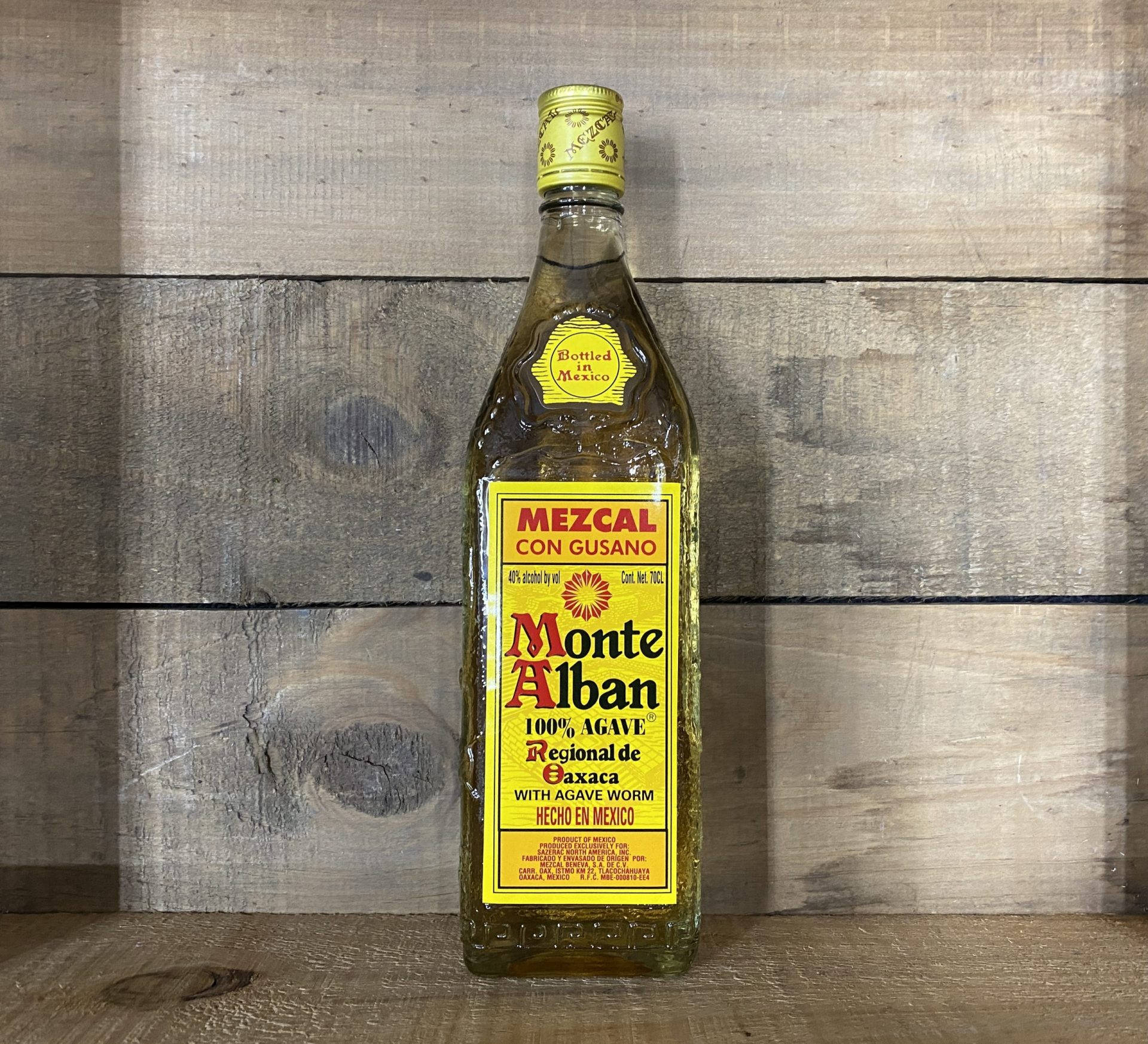 Drink 桌布 壁紙 — 一瓶蒙特阿爾班梅斯卡爾酒連同龍舌蘭蟲，置於質樸木板上，在柔和自然光下居中擺放。