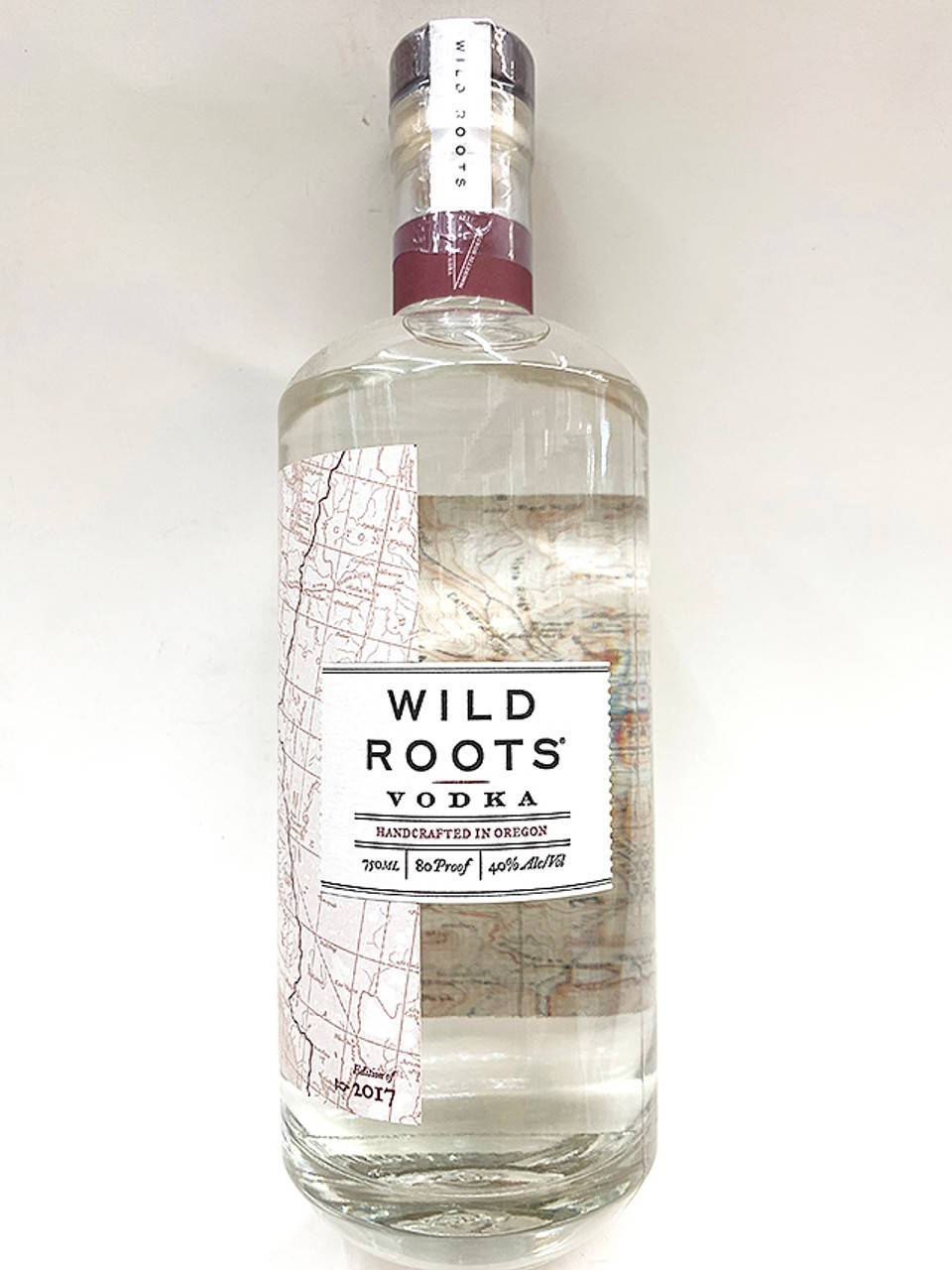 bottle 桌布 壁紙 — 一瓶透明玻璃瓶裝的 Wild Roots Vodka，帶有地圖主題標籤和栗色頸環，立在純白色背景前。