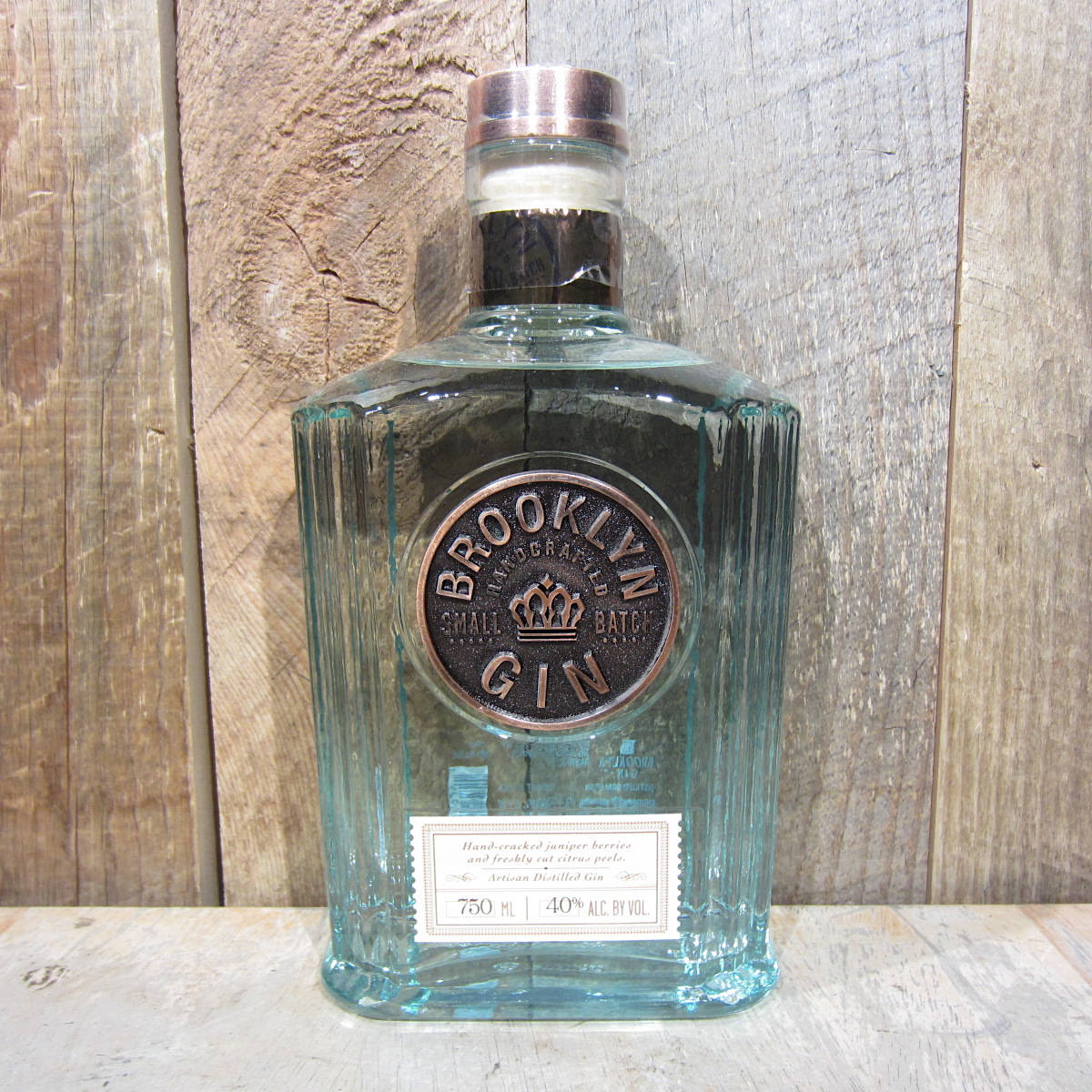 alcohol 桌布 壁紙 — 一瓶透明玻璃瓶裝的布魯克林小批量琴酒，帶有銅蓋和標籤，立於風化木上，背景為質樸的木質背景。