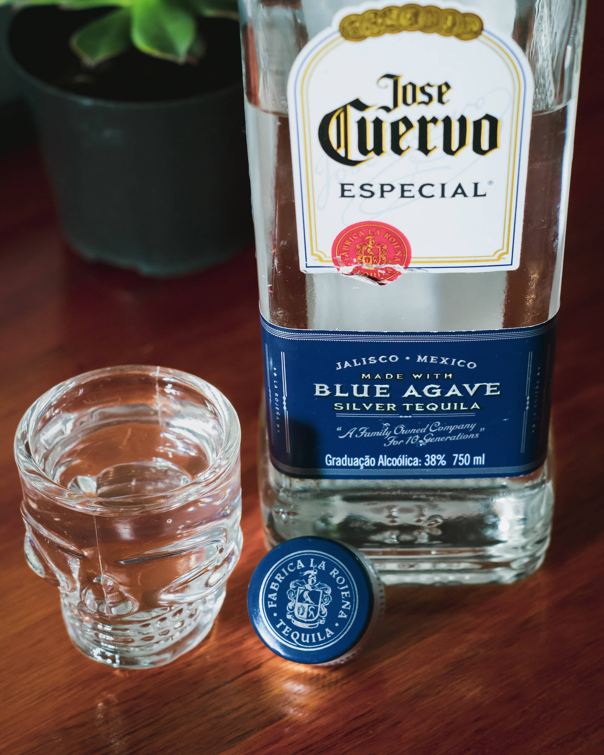 glasses 桌布 壁紙 — 一瓶透明的 Jose Cuervo Especial 龍舌蘭酒放在一個溫暖的木桌上，旁邊有一個骷髏形狀的玻璃杯和它的藍色瓶蓋。