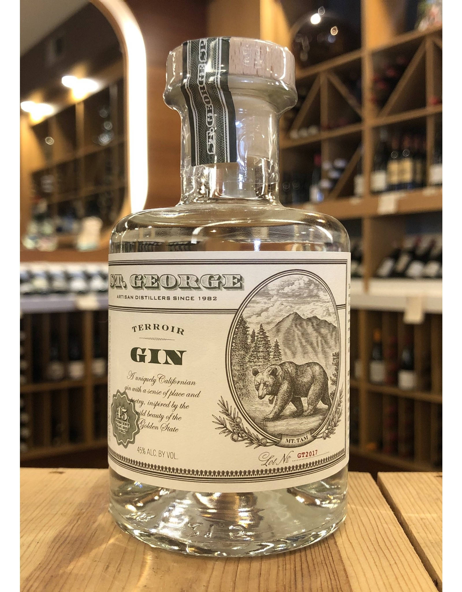 bottle 桌布 壁紙 — 一瓶透明的 St George Terroir Gin，帶有熊的插圖，放在一個燈光溫暖的酒類商店的木桌上。