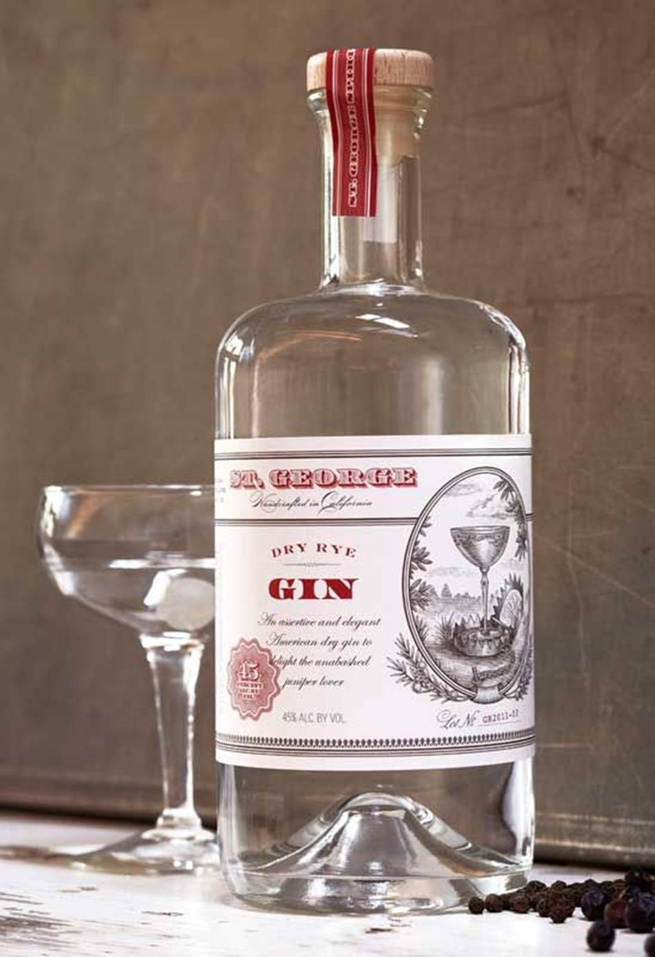 bottle 桌布 壁紙 — 一瓶透明的 St George Dry Rye Gin，帶有復古標籤，旁邊放著一個空的 coupe 杯，放在質樸的木質表面上。