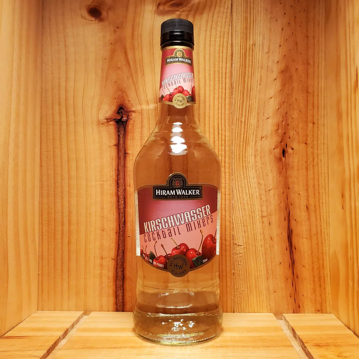 alcohol 桌布 壁紙 — 一瓶透明的Hiram Walker Kirschwasser雞尾酒調和器，帶有櫻桃圖案，置於木架中央，背景為溫暖的木鑲板。