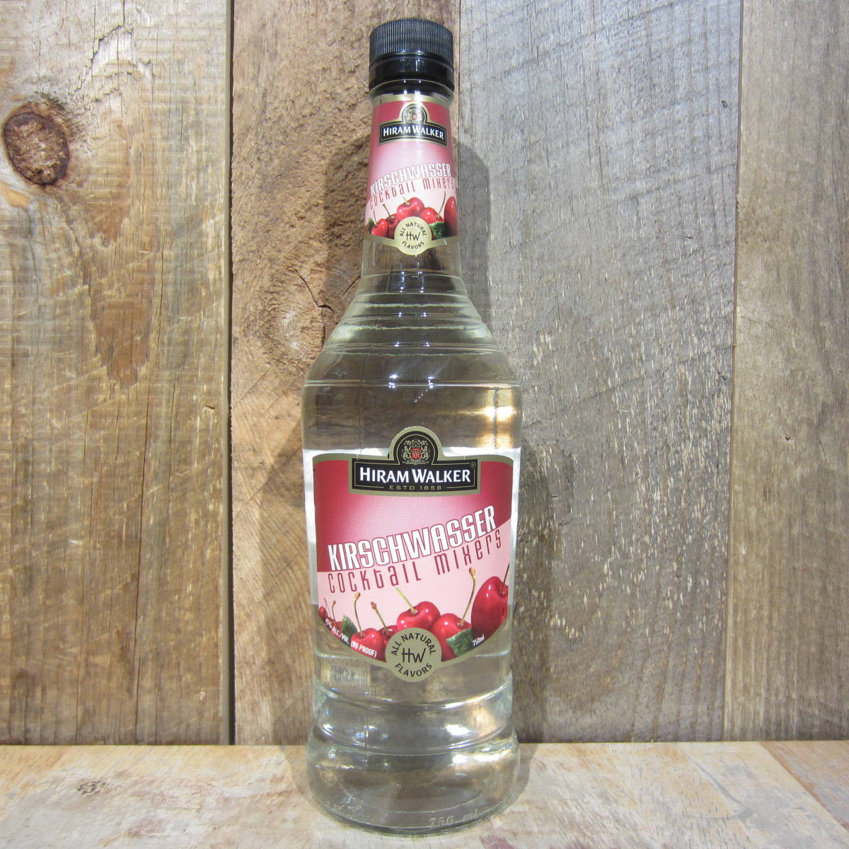alcohol 桌布 壁紙 — 一瓶透明的Hiram Walker Kirschwasser雞尾酒調和器，帶有櫻桃圖案，立在質樸的木質背景前。
