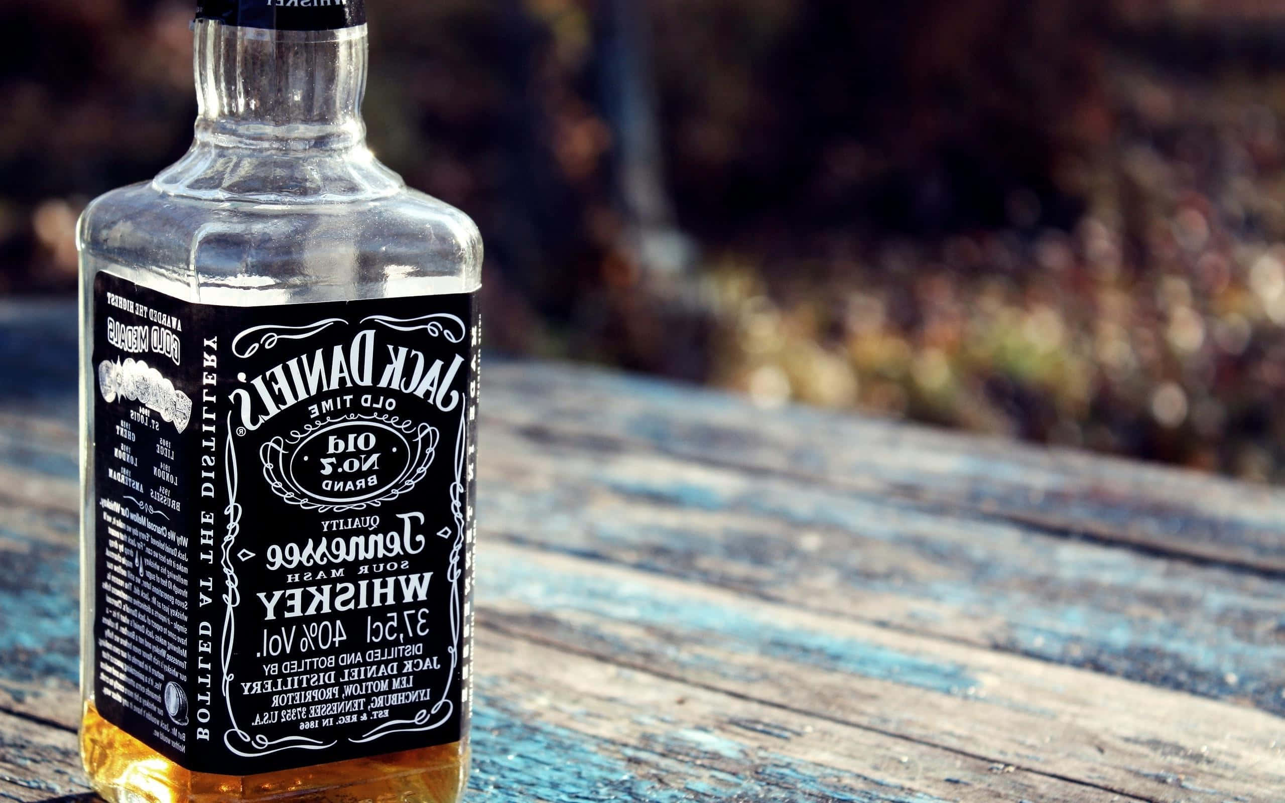 alcohol 桌布 壁紙 — 一瓶透明的Jack Daniel's威士忌放在一張風化的藍色木桌上，背景是模糊的秋景。
