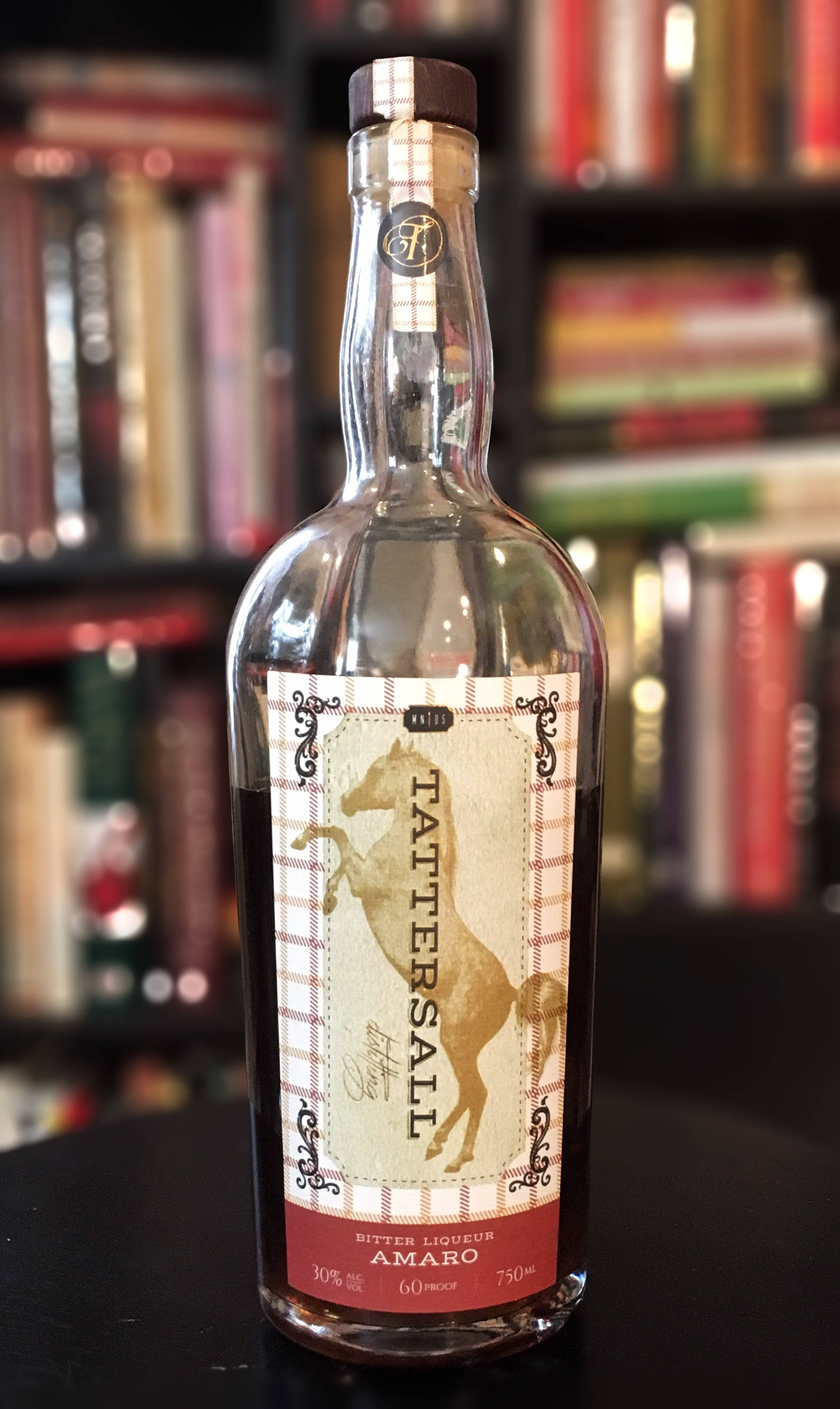 飲料 桌布 壁紙 — 一瓶透明的Tattersall苦味利口酒amaro放在深色桌子中央，背景是模糊的書架。
