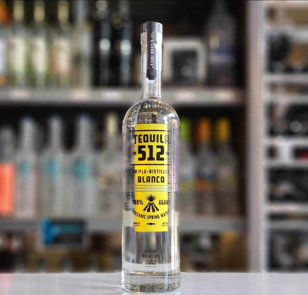 drinks 桌布 壁紙 — 一瓶透明的Tequila 512 Blanco，帶有鮮明的黃色標籤，放在吧檯中央，背景是柔和模糊的酒架。