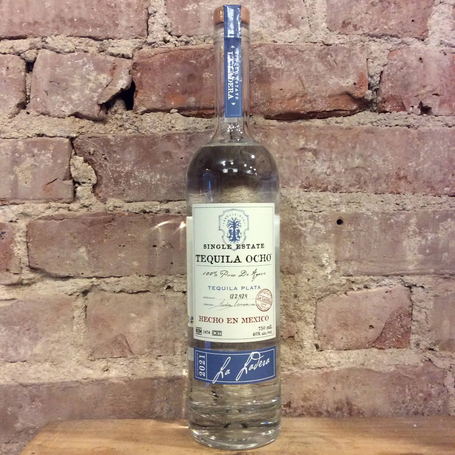 bottle 桌布 壁紙 — 一瓶透明的Tequila Ocho酒瓶放在木質表面上，背景是風化的紅磚牆。