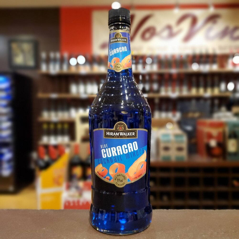 alcohol 桌布 壁紙 — 一瓶鮮藍色的Hiram Walker Blue Curacao雞尾酒調和劑醒目地放在吧檯上，背景是模糊的酒架。