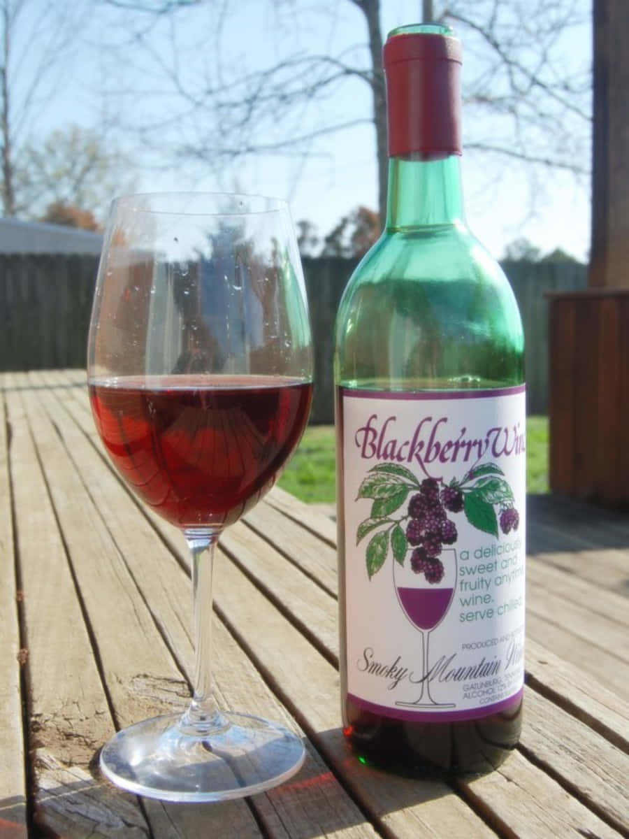 Blackberry Wine 桌布 壁紙 — 一瓶黑莓酒和一杯紅酒放在陽光下風化的木甲板上。
