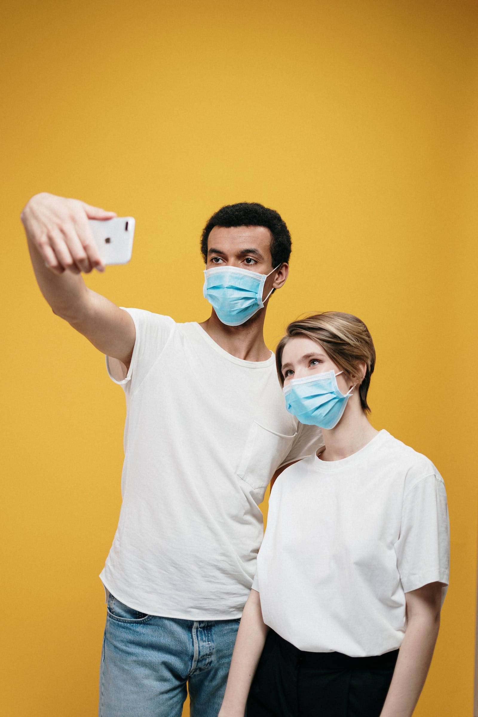 Love iPhone 桌布 壁紙 — 一男一女戴著藍色外科口罩，在純芥末黃色背景前自拍。