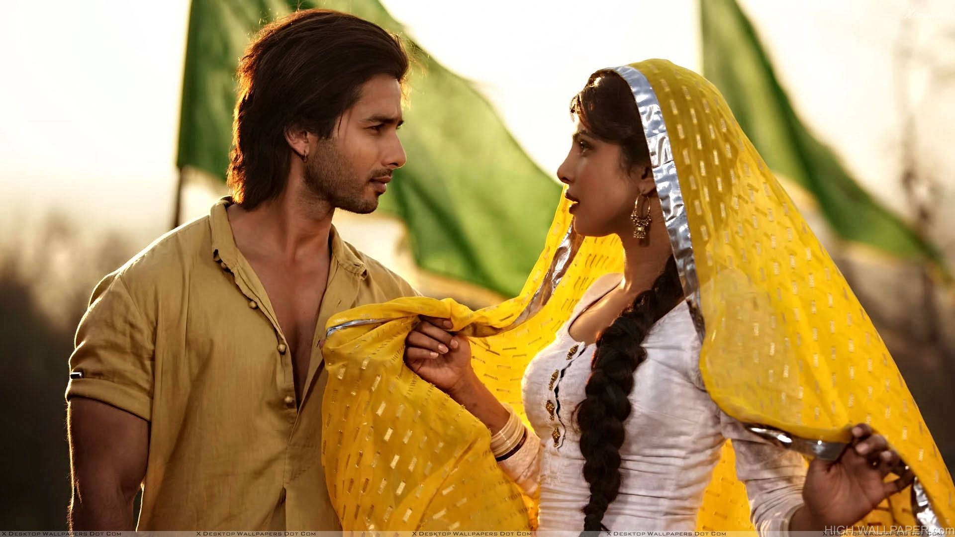 Shahid Kapoor 桌布 壁紙 — 一男一女穿著傳統服飾，在溫暖的金色光芒下共享親密時刻，身後有綠色旗幟。