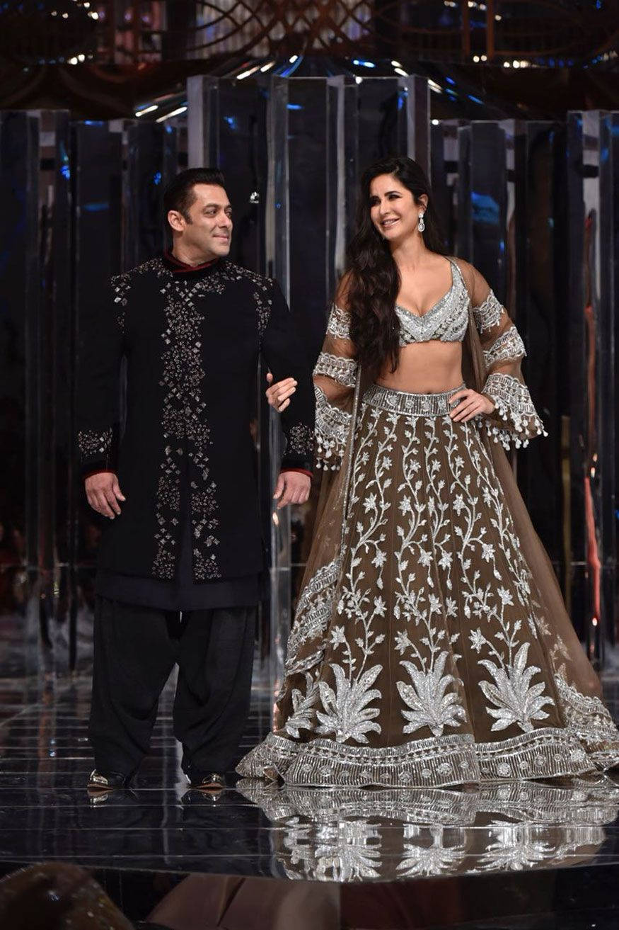 salman khan HD 桌布 壁紙 — 一男一女穿著華麗的傳統印度服裝，在戲劇性燈光下手牽手走在反射的舞台上。