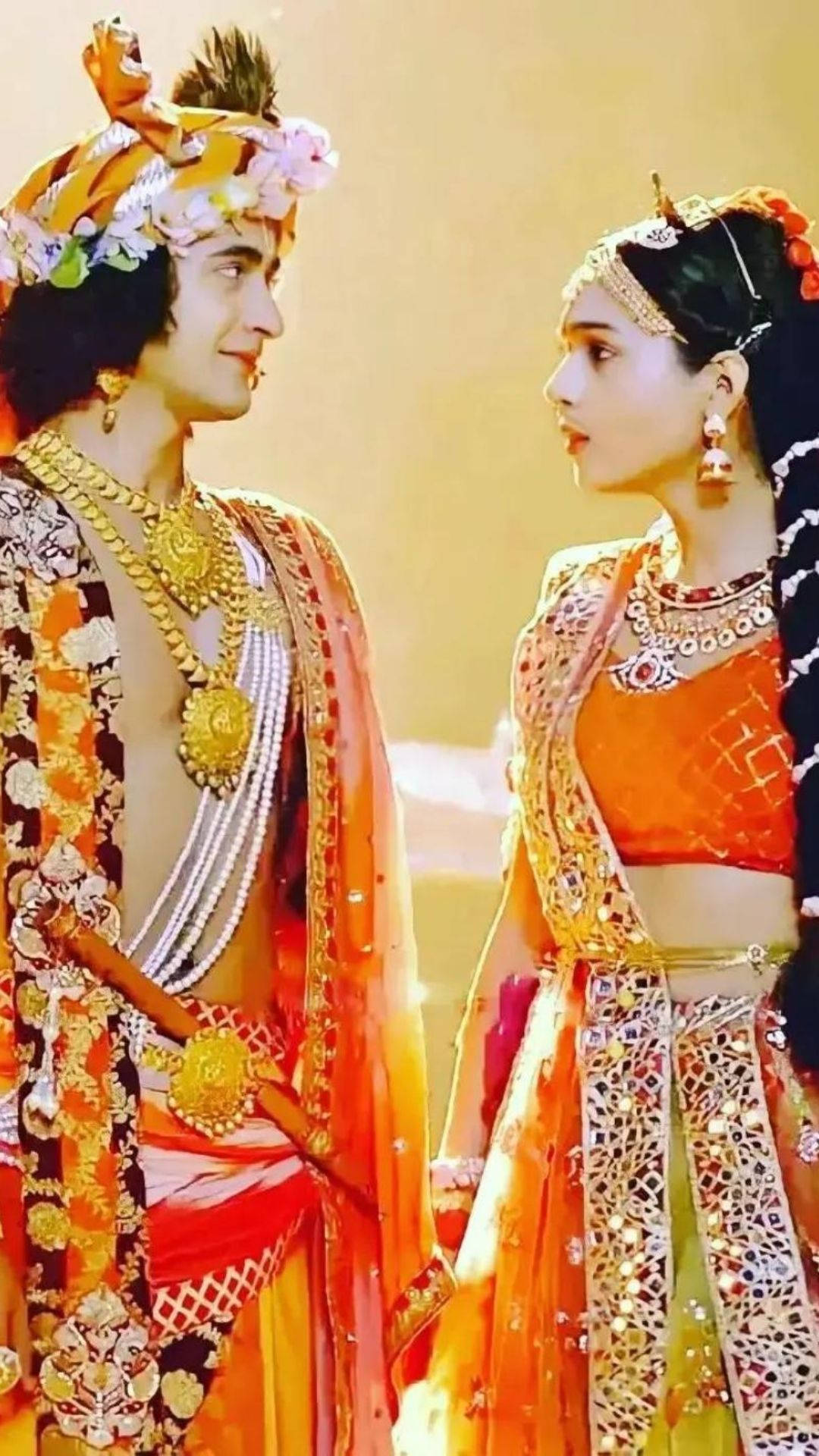 radha krishna serial 桌布 壁紙 — 一男一女穿著華麗的傳統印度服飾，在溫暖的金色背景下深情對望。