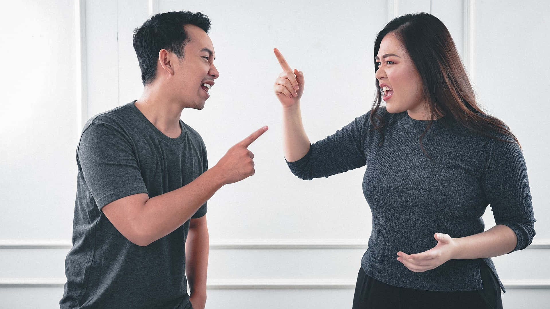 rude 桌布 壁紙 — 一男一女身穿深灰色襯衫，在光線明亮的簡約房間內面對面爭論，互相指責。