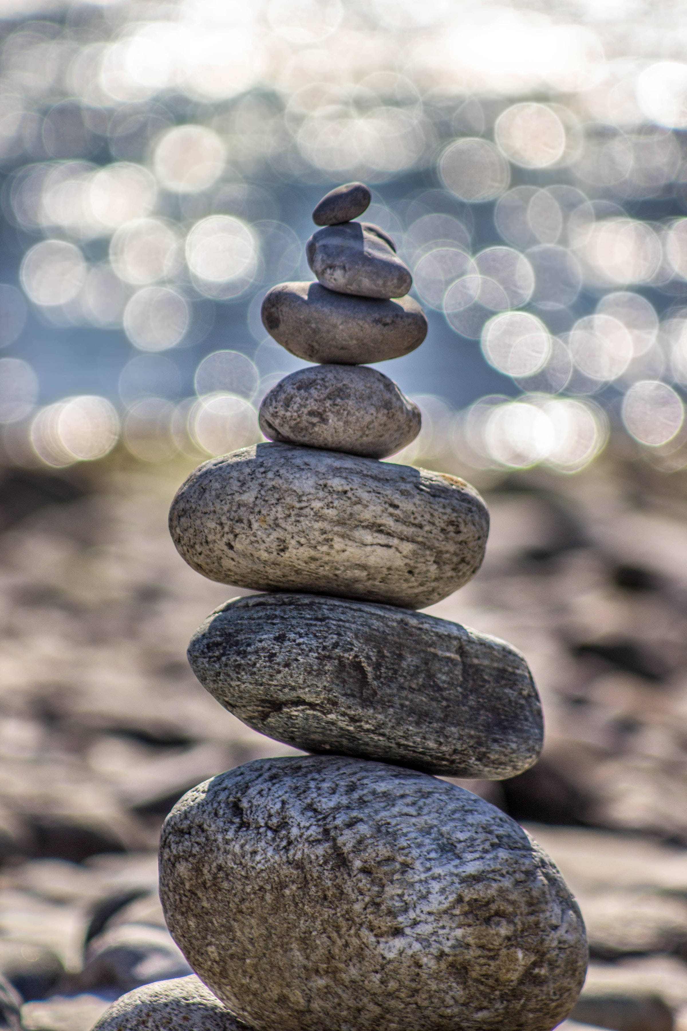 Stone 桌布 壁紙 — 一疊光滑的河石在陽光明媚的海灘上完美平衡，背景是閃爍的水波散景。