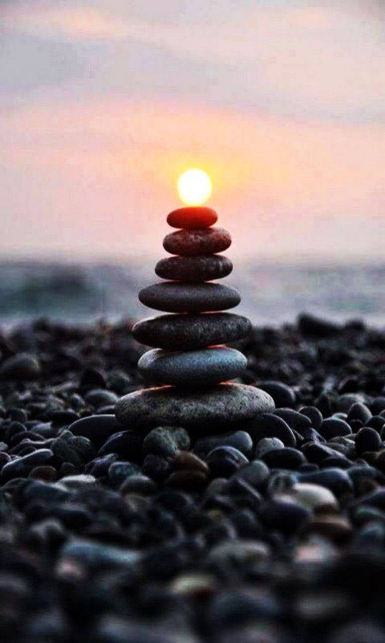 禪 桌布 壁紙 — 一疊光滑的石頭在卵石海灘上保持平衡，夕陽在後方落下，散發出溫暖的光芒。