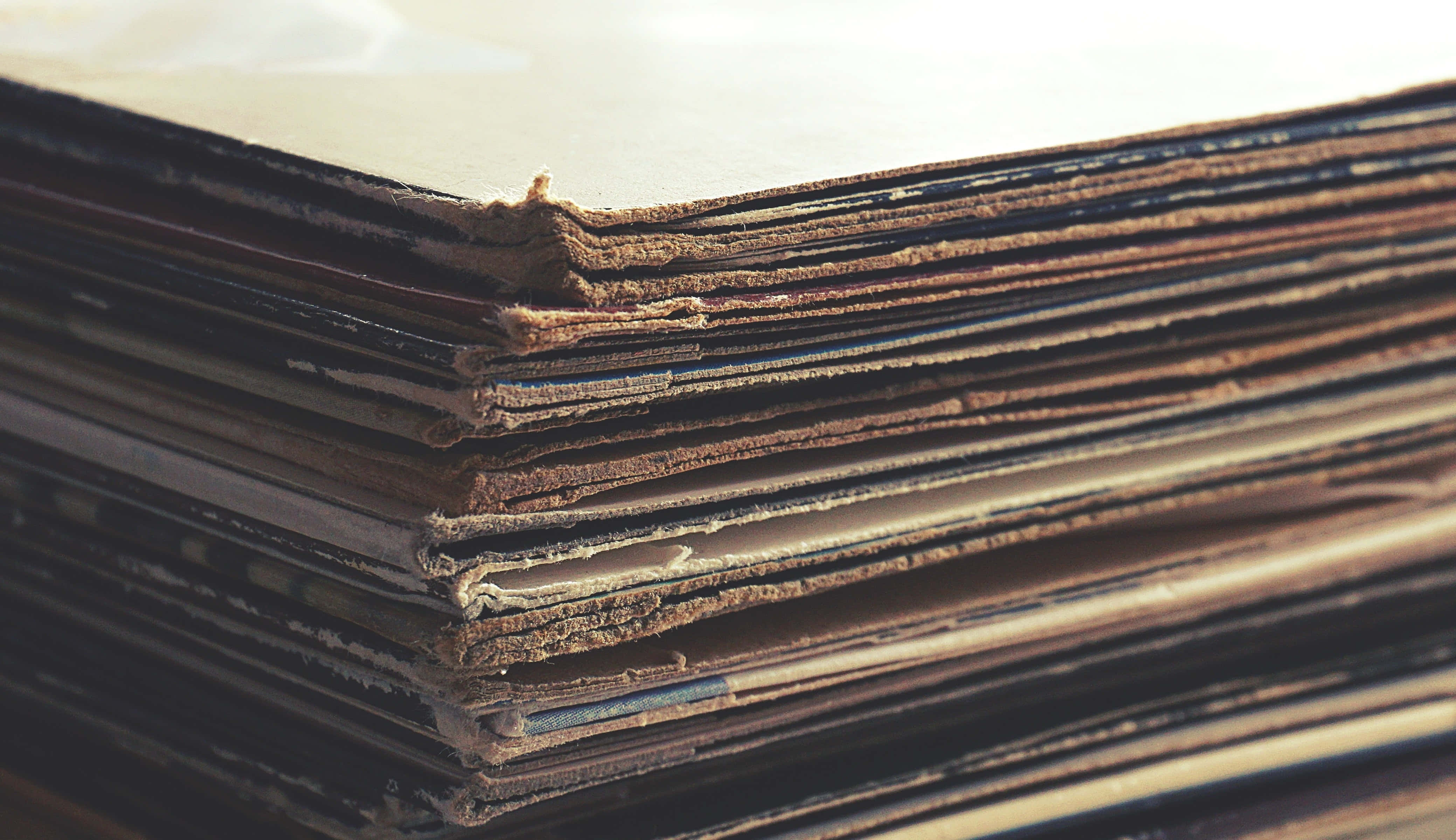 cardboard 桌布 壁紙 — 一疊厚厚的復古黑膠唱片的特寫，邊緣磨損，標籤褪色，沐浴在溫暖的陽光下。