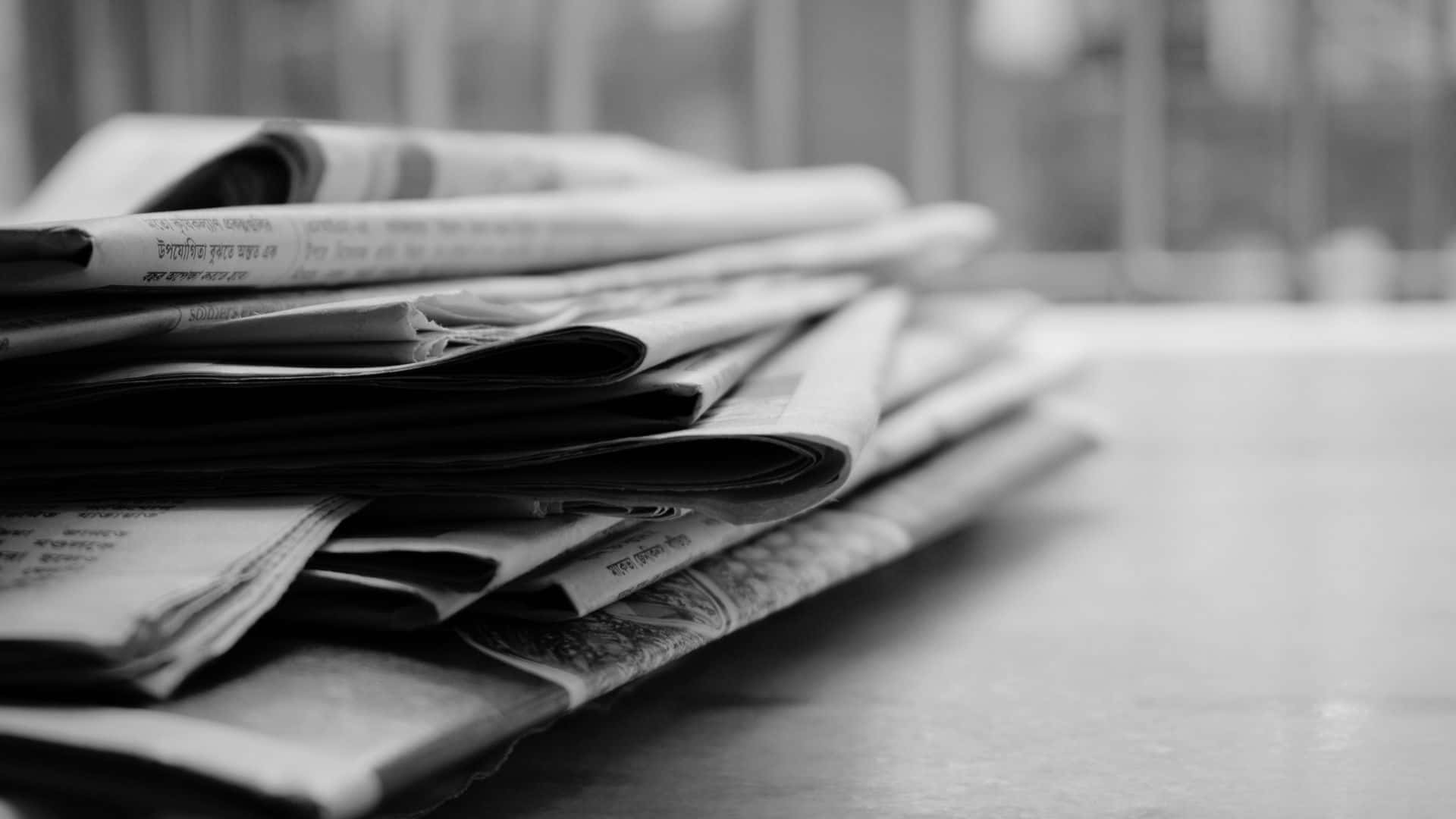 Black And White Newspaper 桌布 壁紙 — 一疊單色折疊報紙放在光滑表面上，背景模糊。