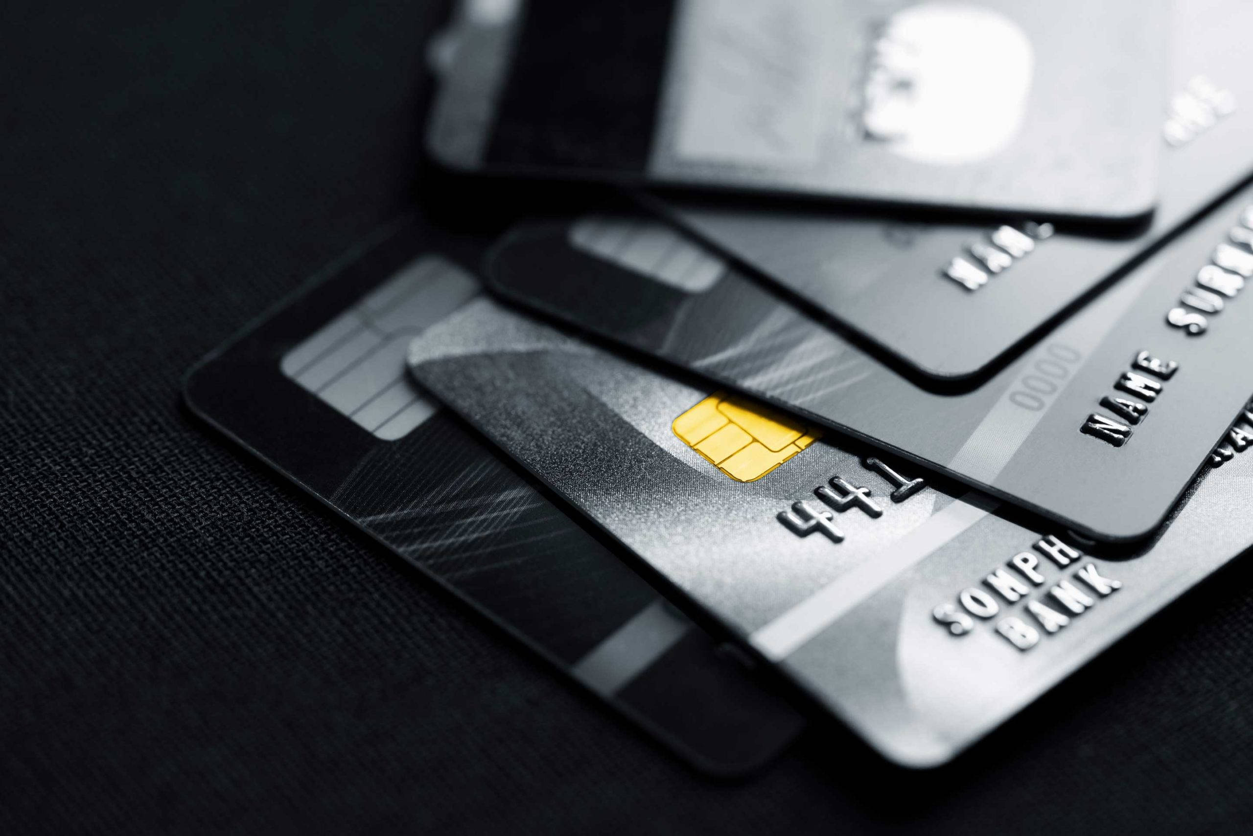 Credit Card 桌布 壁紙 — 一疊時尚黑色和銀色信用卡，帶有金色晶片，放置在深色紋理表面上。