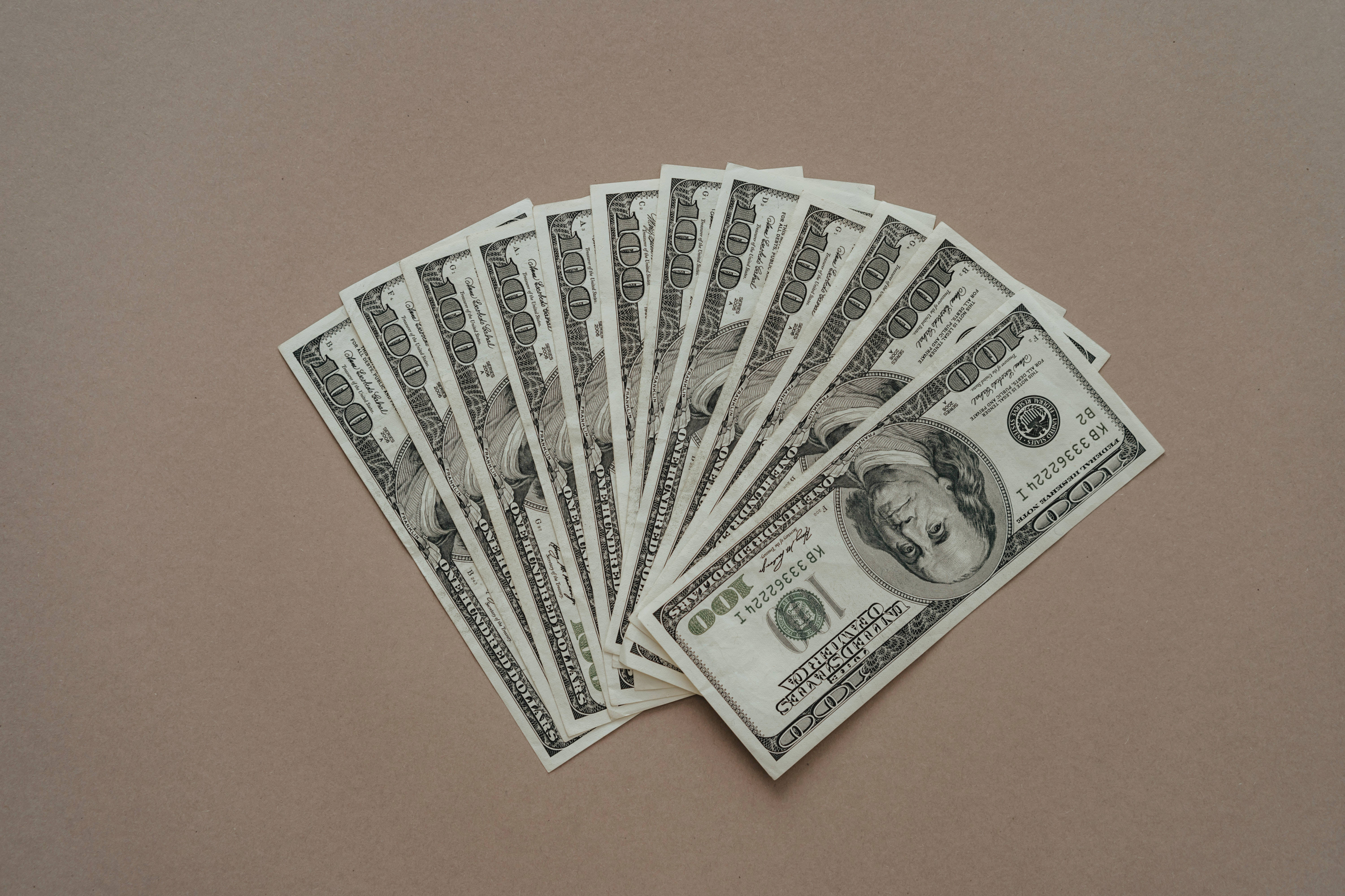 金錢 桌布 壁紙 — 一疊清脆的百元美鈔扇狀散佈在柔和的棕色表面上。