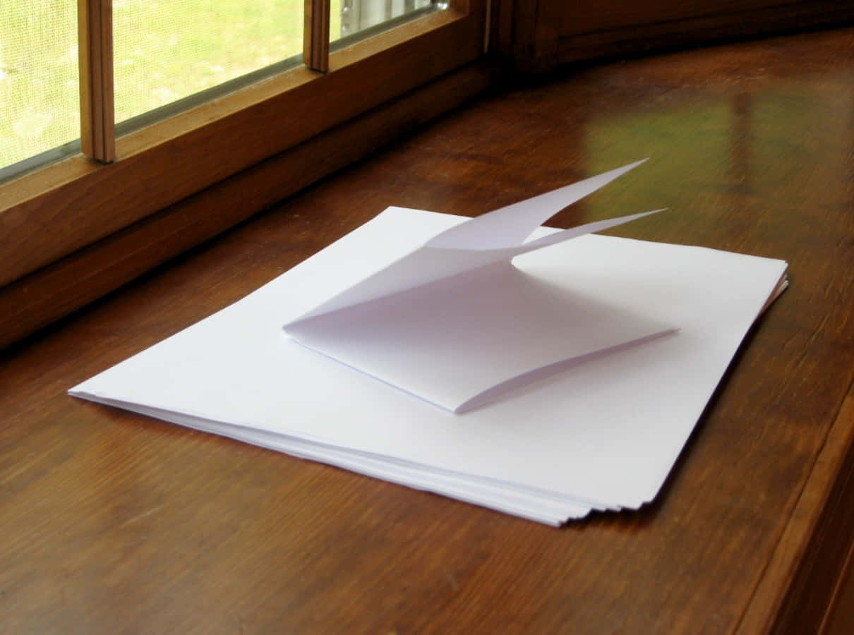 paper 桌布 壁紙 — 一疊潔白清脆的紙張，上面放著一隻摺好的摺紙鶴，擱在溫暖的木窗台上，沐浴在柔和自然光中。
