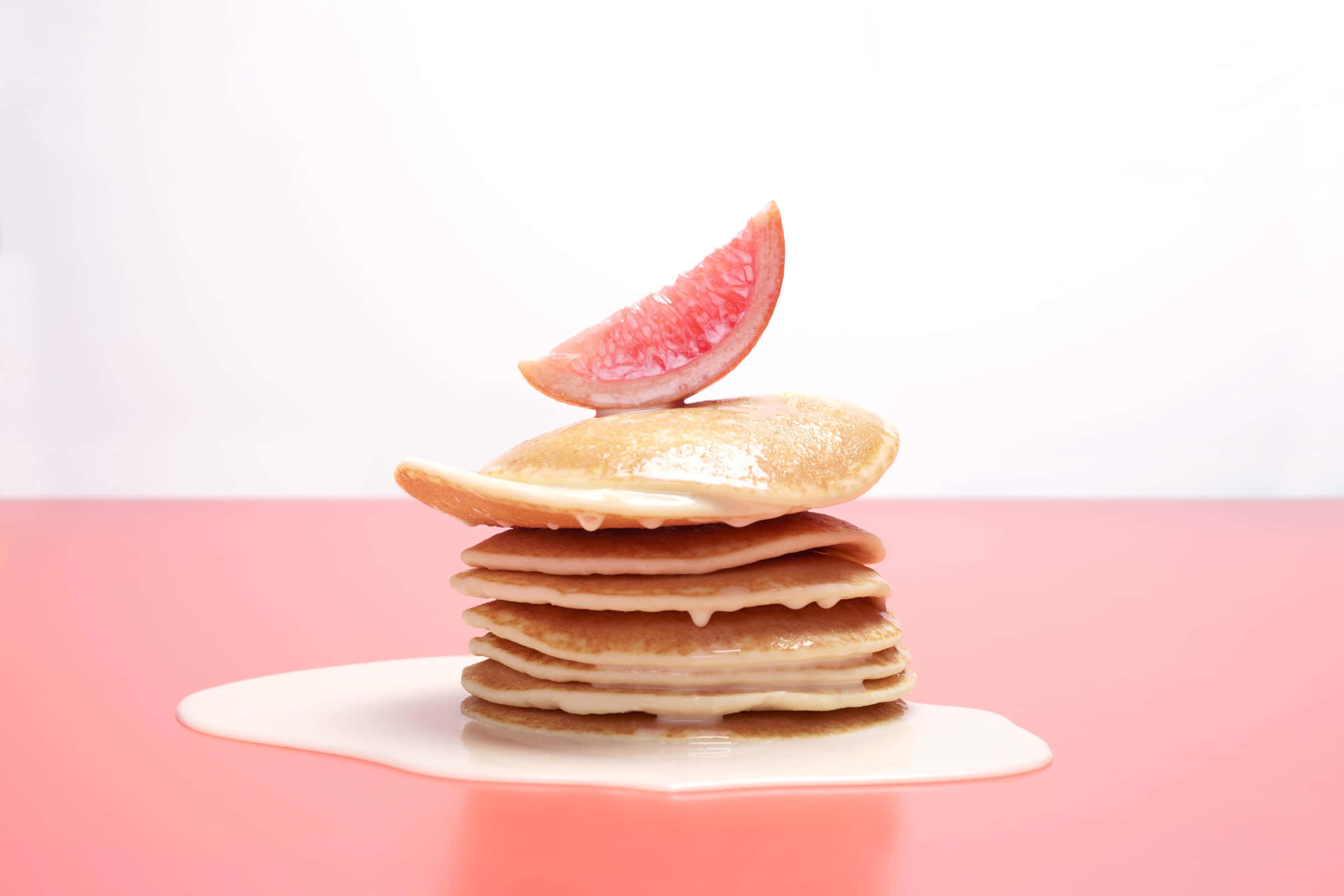 Desserts 桌布 壁紙 — 一疊高高的金黃色鬆餅，淋上糖漿，上面放著一片粉紅葡萄柚，置於粉紅色表面上。