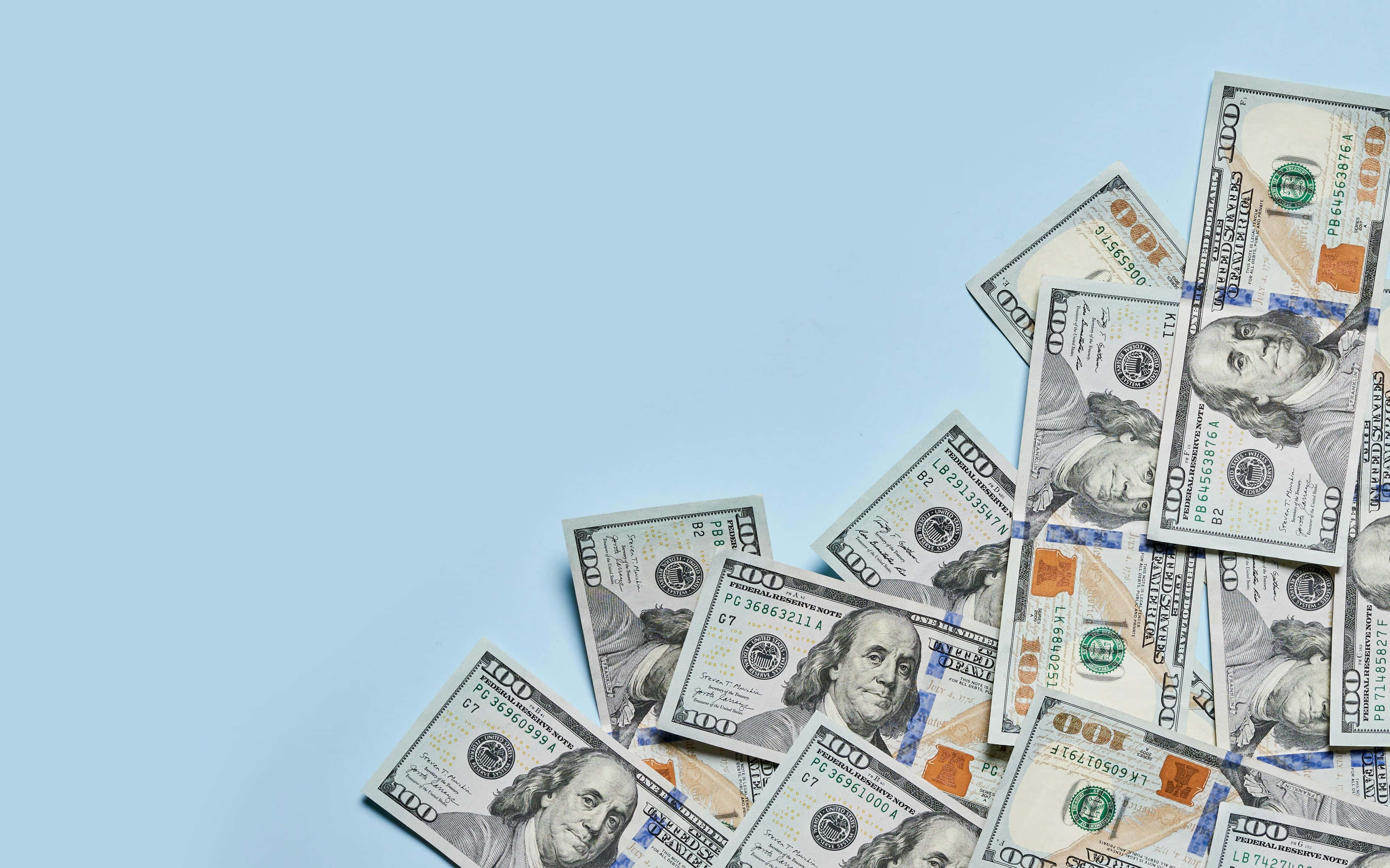 100 Dollar Bill 桌布 壁紙 — 一百美元鈔票對角散落在純淺藍色背景上，留有大量負空間。