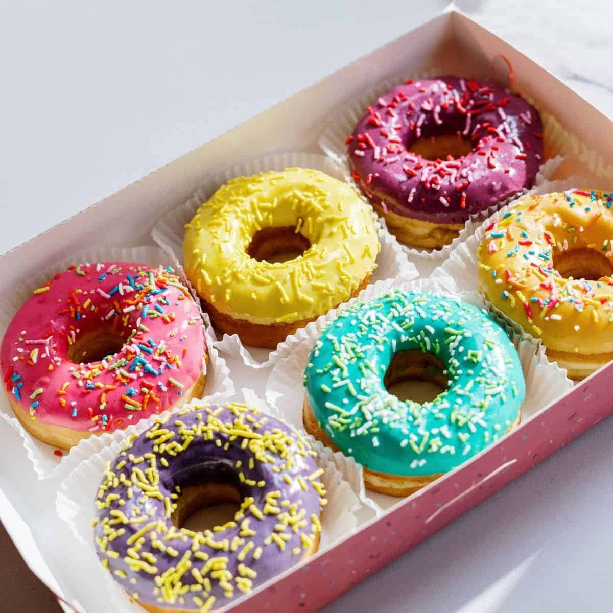 Glazed Donut 桌布 壁紙 — 一盒六個色彩鮮豔的釉面甜甜圈，上面有彩色糖粒，整齊地排列在獨立的紙杯中。