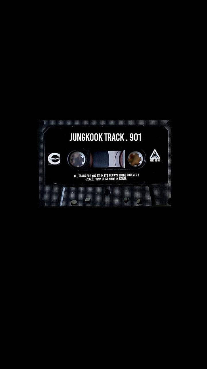 Bts Aesthetic 桌布 壁紙 — 一盒復古黑色卡式錄音帶，中央印有「JUNGKOOK TRACK . 901」字樣，置於帶有像素紋理的漆黑背景上。