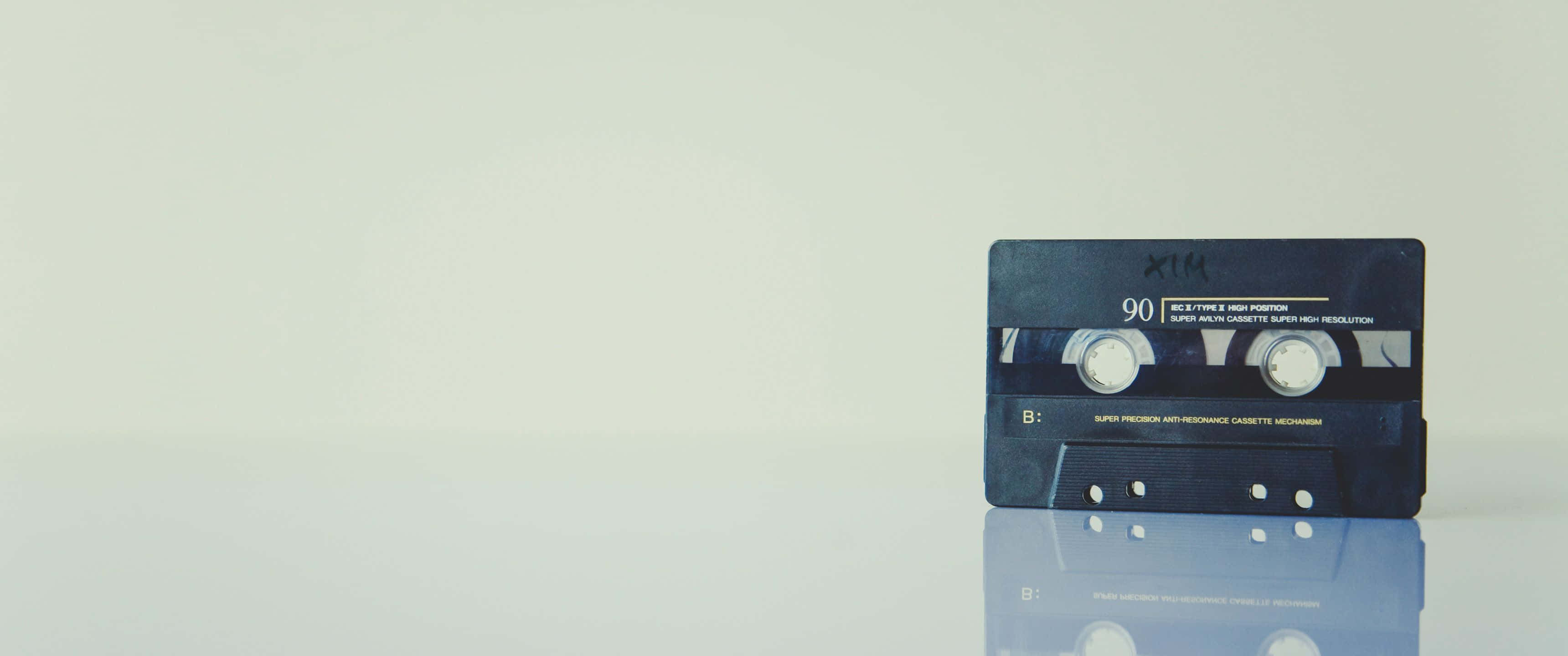 Mixtape 桌布 壁紙 — 一盒復古黑色錄音帶放在反光的白色表面上，背景是柔和的米白色。