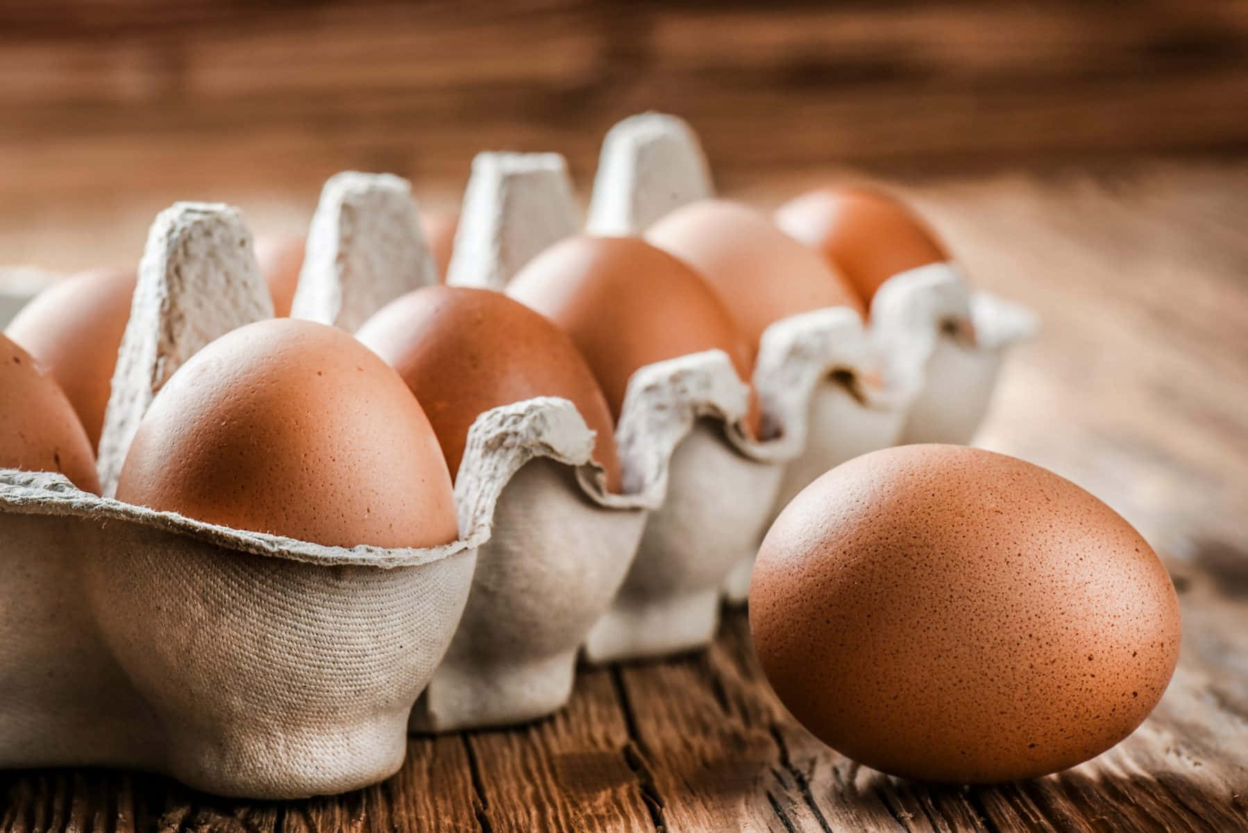 Egg 桌布 壁紙 — 一盒棕色雞蛋放在質樸的木桌上，旁邊放著一個雞蛋。