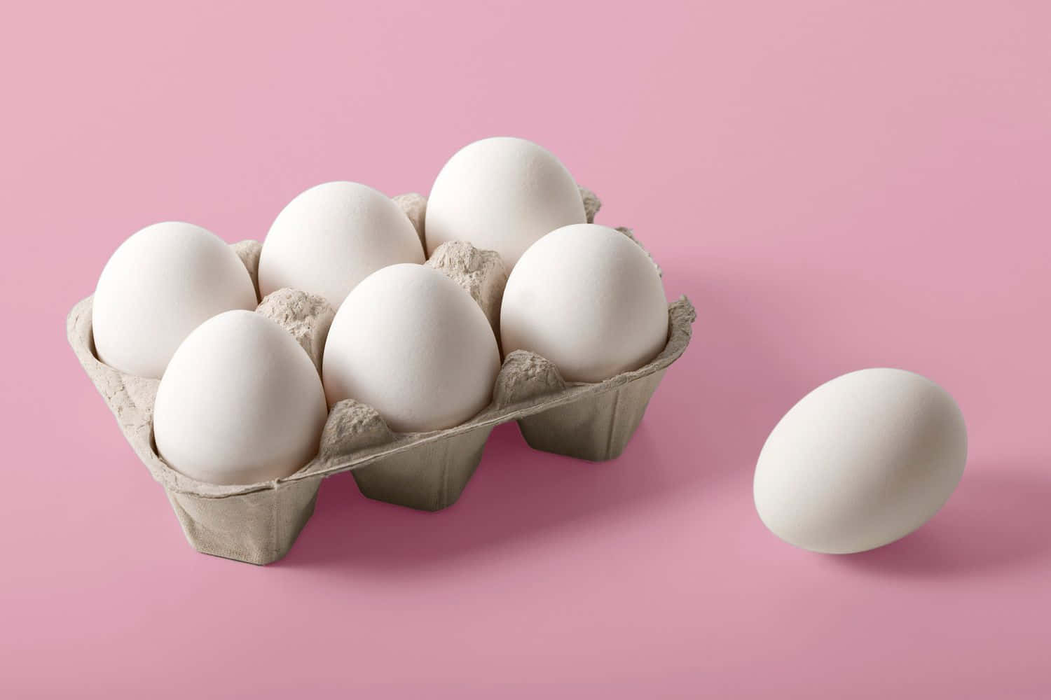 Eggs 桌布 壁紙 — 一盒白色雞蛋放在柔軟的粉紅色背景上，旁邊放著一顆雞蛋。