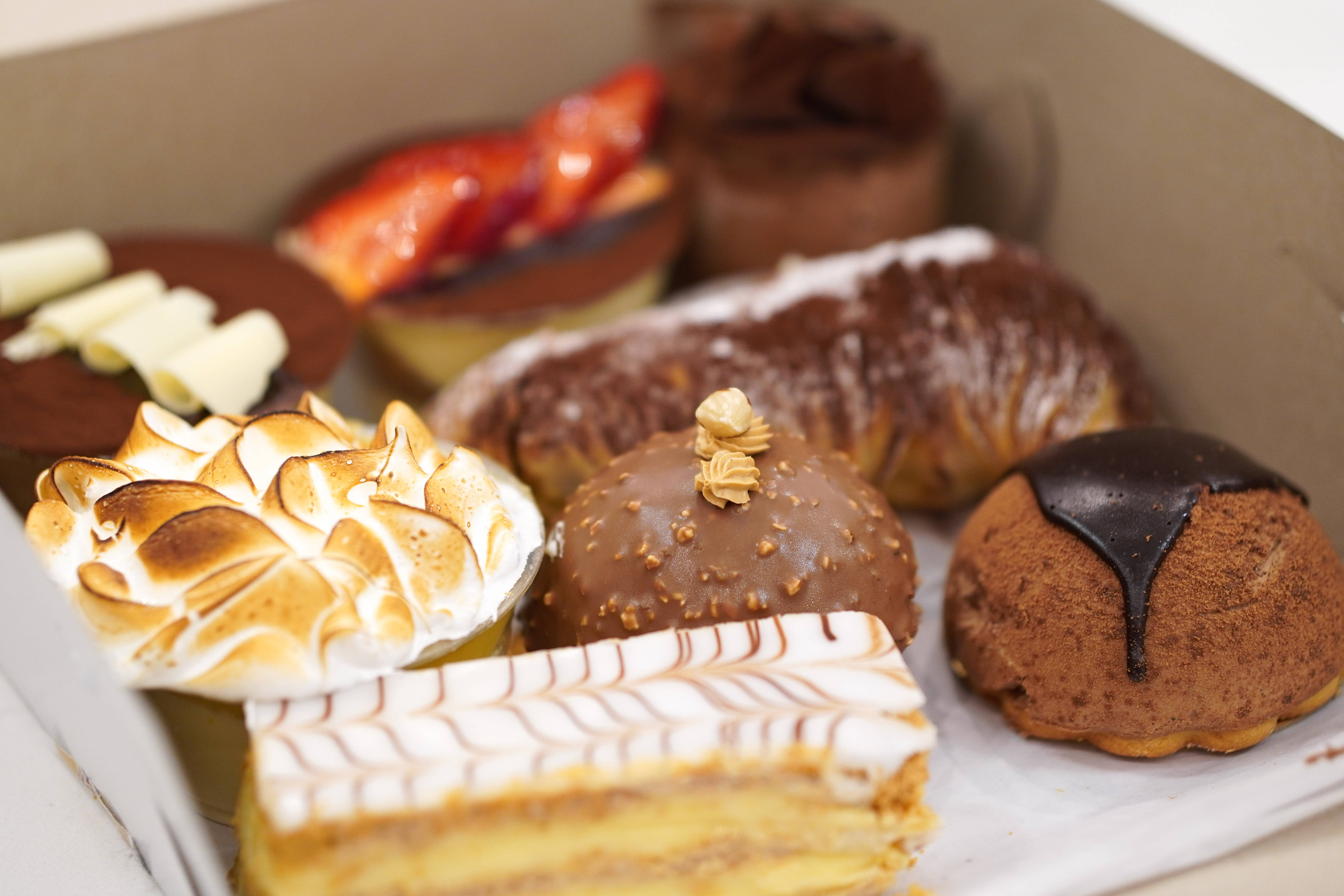 Pastries 桌布 壁紙 — 一盒誘人的美食糕點，包括蛋白霜甜點、巧克力釉面美食和多層蛋糕，裝在紙板盒中。