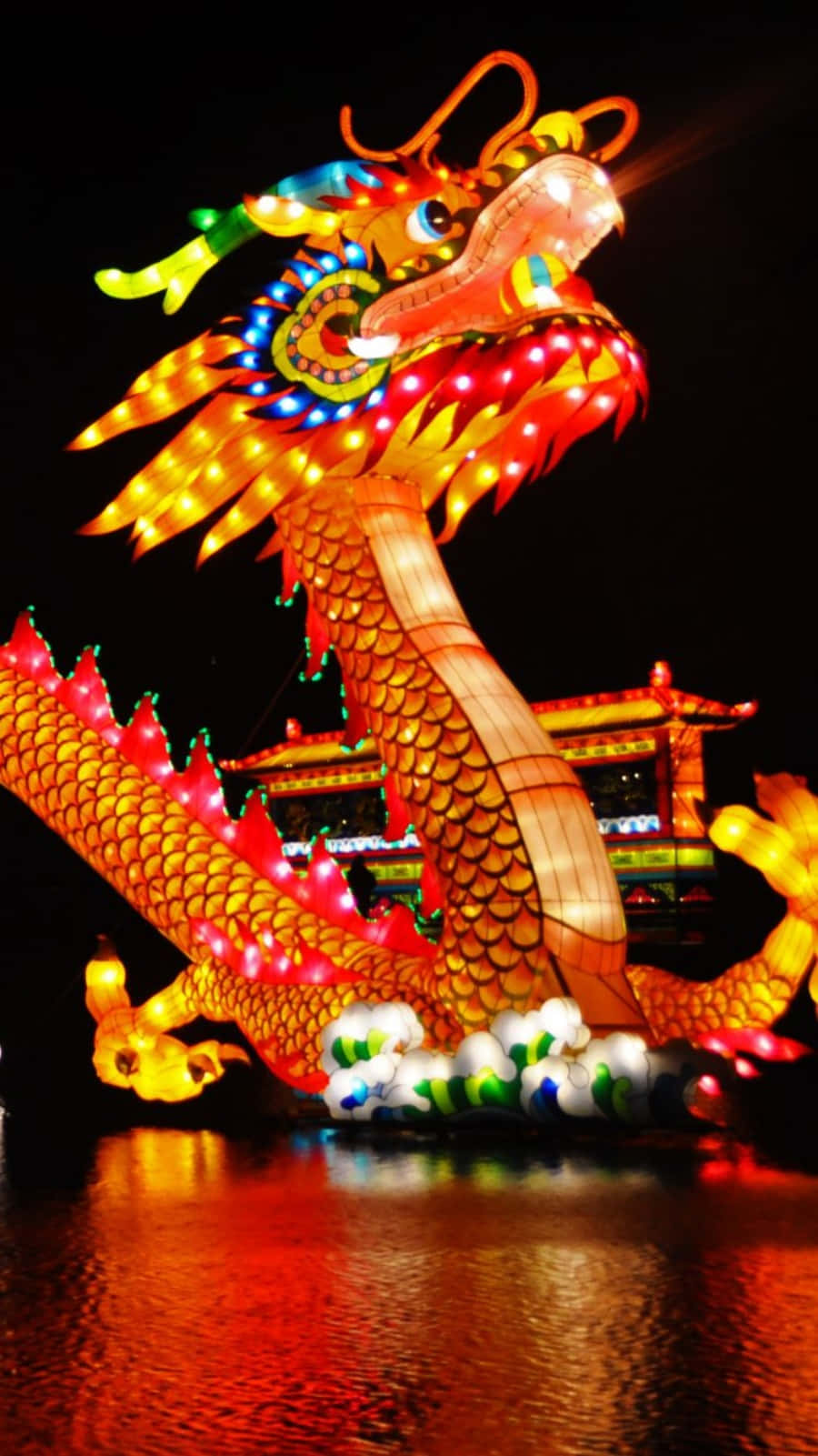 桌布 壁紙 — 一盞充滿活力的發光龍燈在夜間滑過水面，色彩繽紛的燈光在水面上反射。
