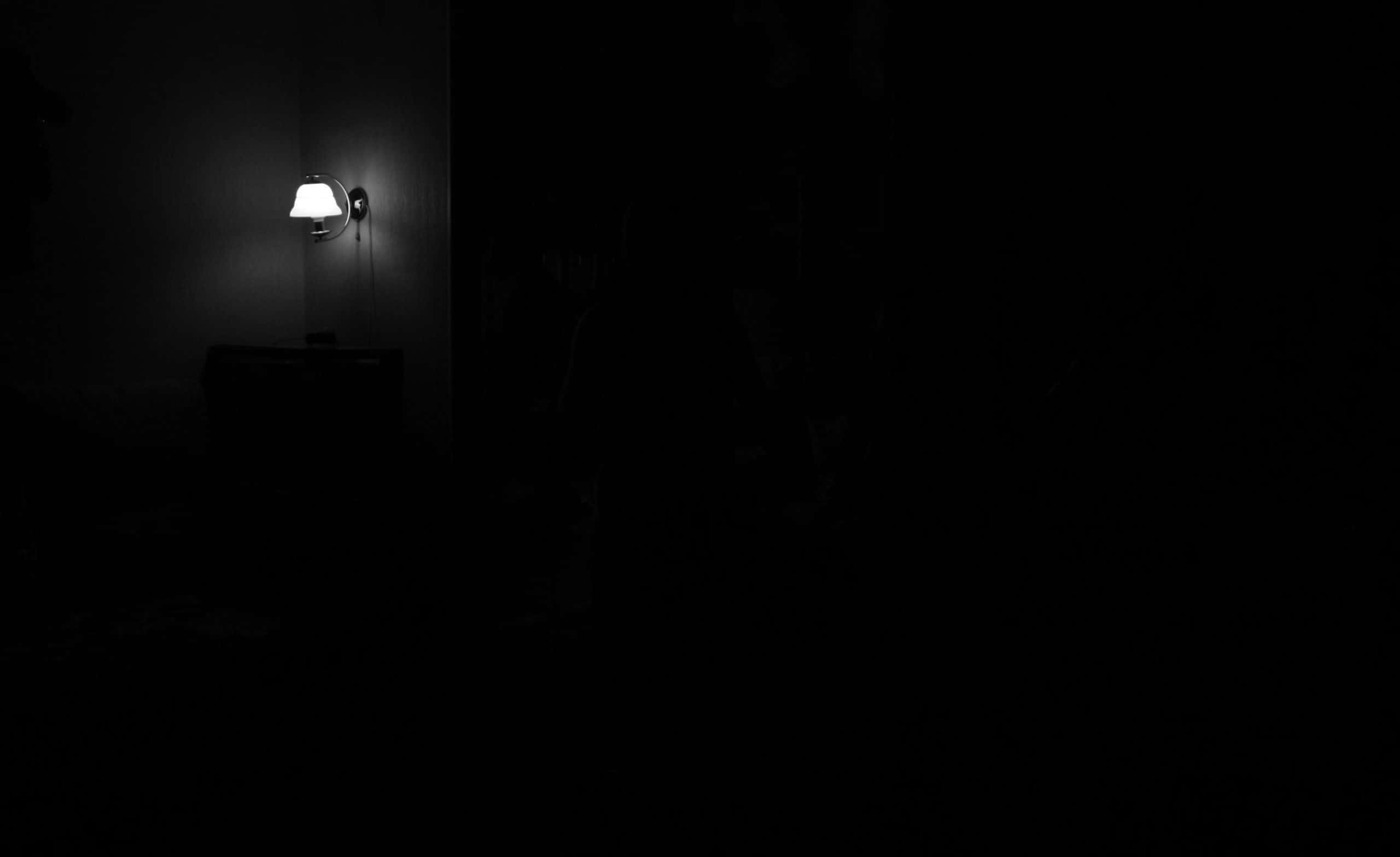 Dark Corner 桌布 壁紙 — 一盞壁燈在漆黑的房間中散發出柔和的光芒，營造出深邃的陰影和高對比度。