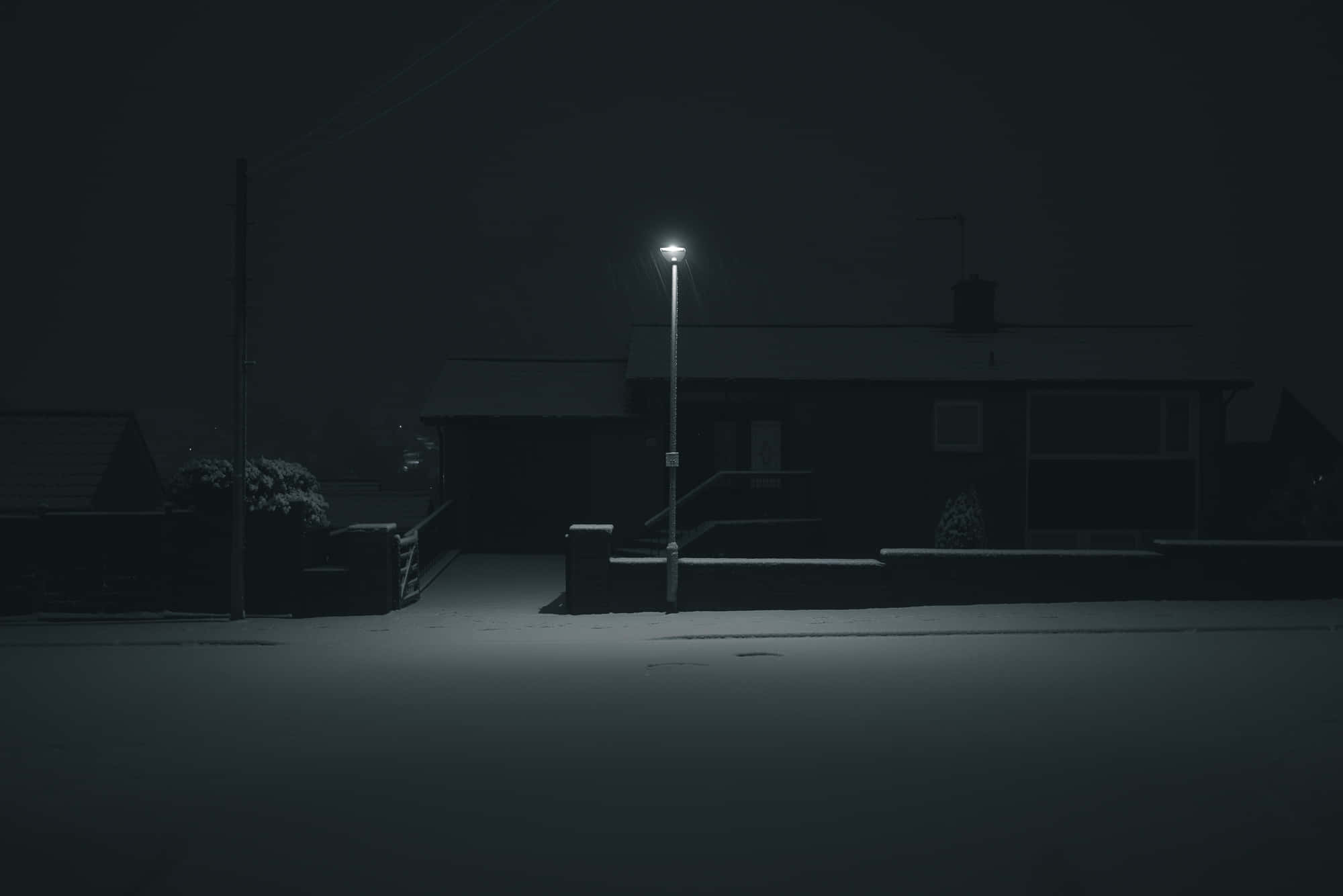 黑夜 桌布 壁紙 — 一盞孤獨的路燈在夜晚將柔和的光芒投射在積雪的郊區街道上，照亮了黑暗中的寧靜房屋。
