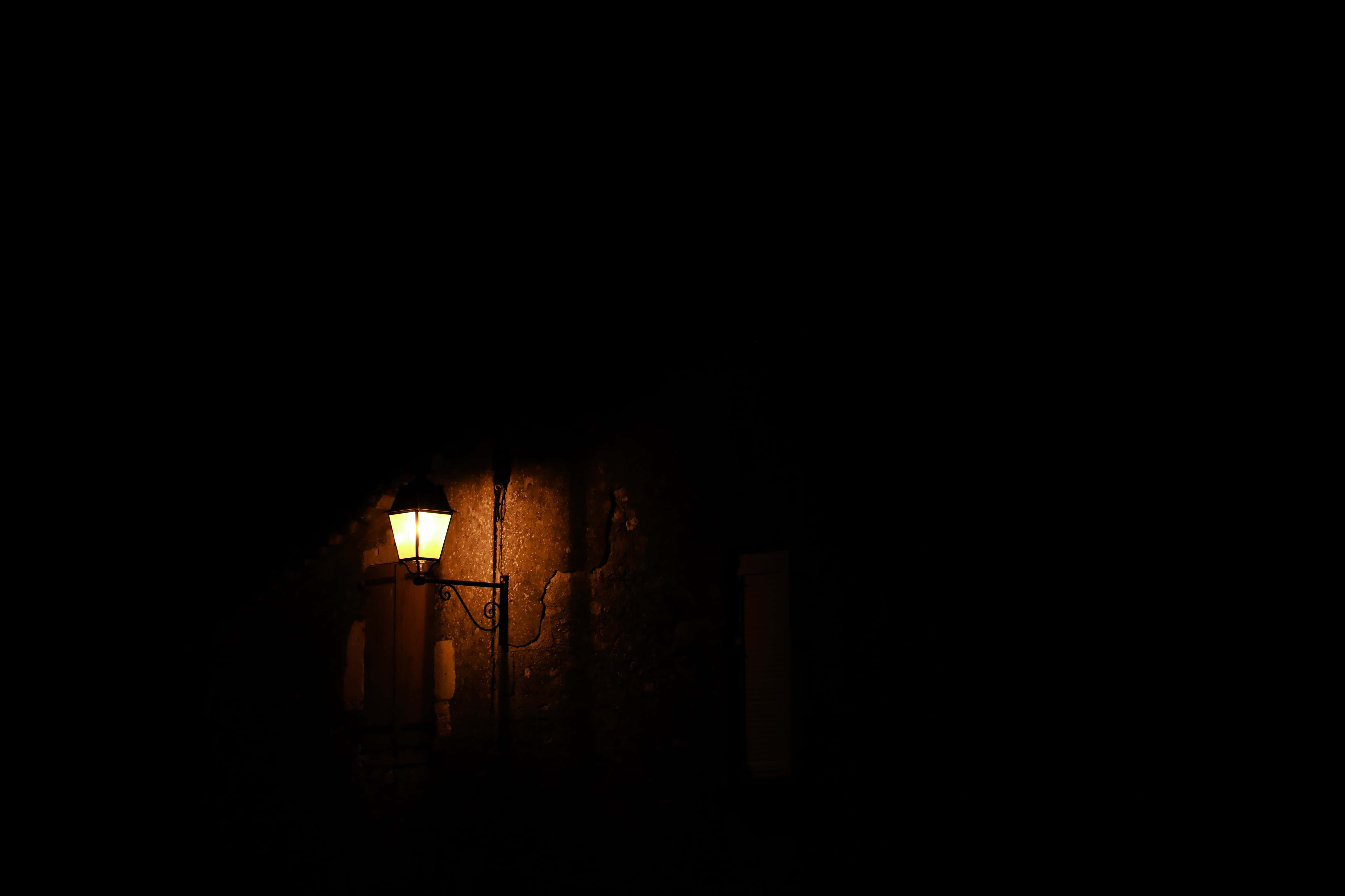 Dark Theme 桌布 壁紙 — 一盞復古路燈在深夜的黑暗中，將溫暖的光芒投射在有紋理的石牆上。