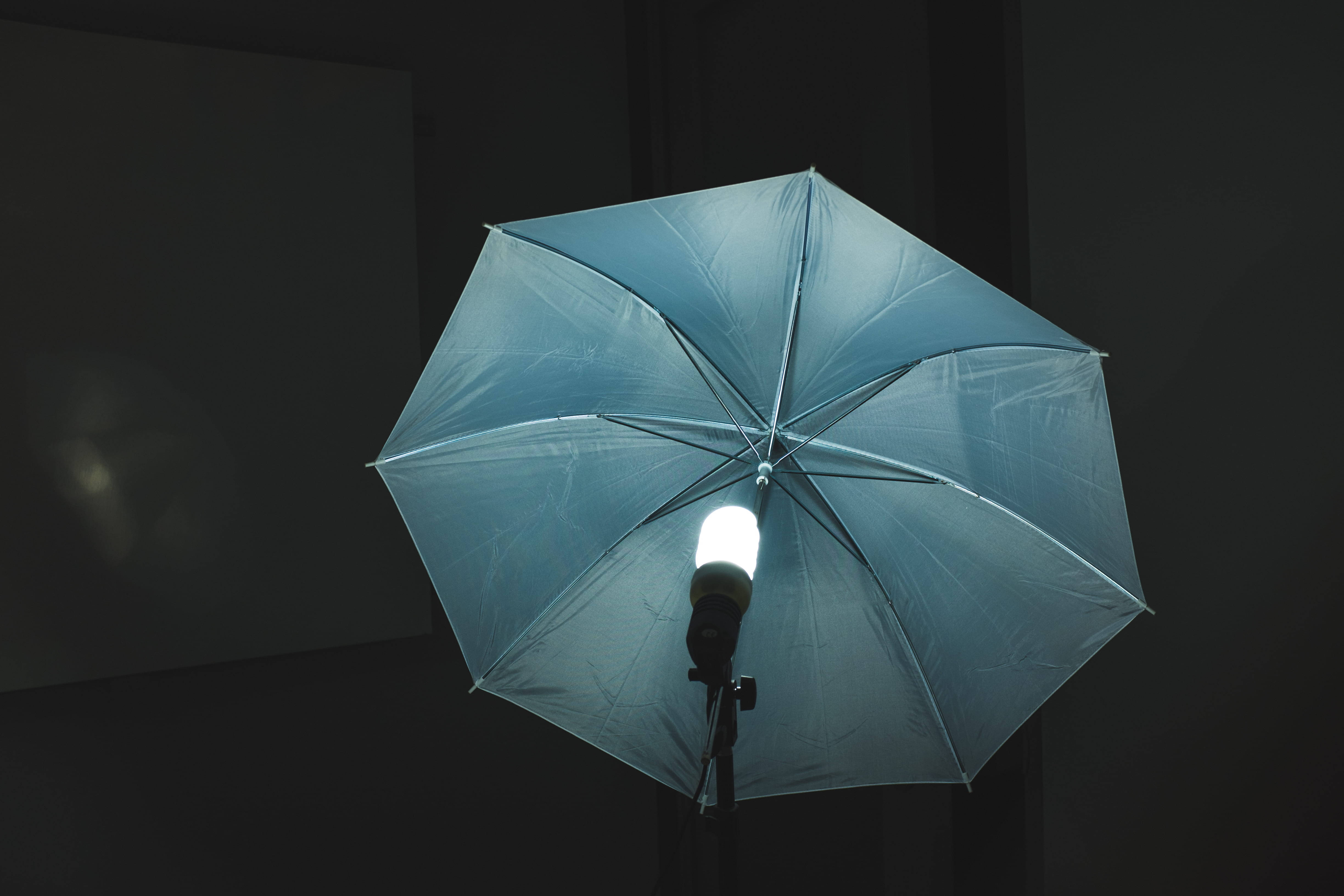 Studio 桌布 壁紙 — 一盞攝影棚燈光穿過半透明藍色雨傘，照射在深色背景上。
