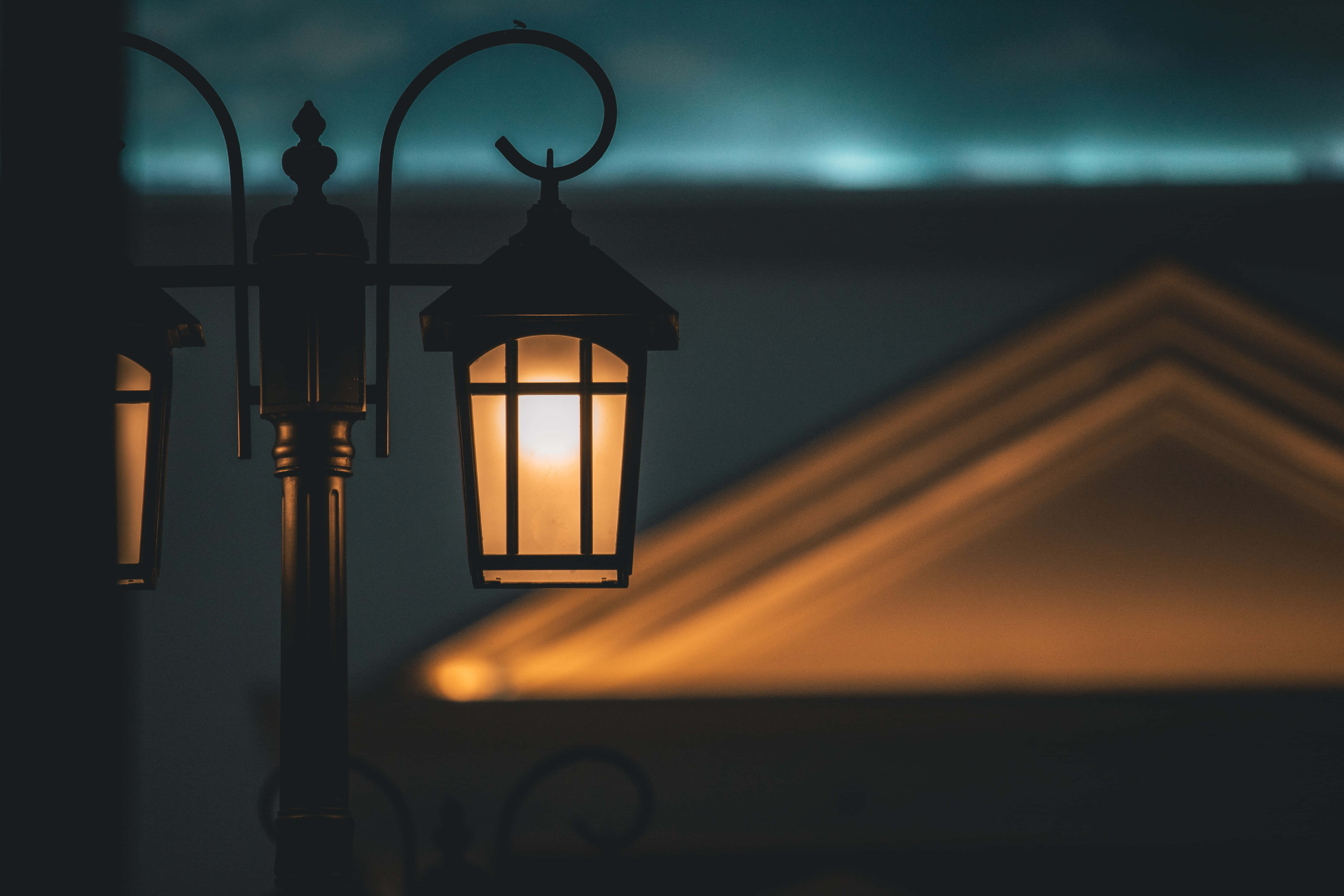Street Light 桌布 壁紙 — 一盞發光的復古街燈在昏暗的暮色天空和模糊的建築物剪影中投射出溫暖的光芒。