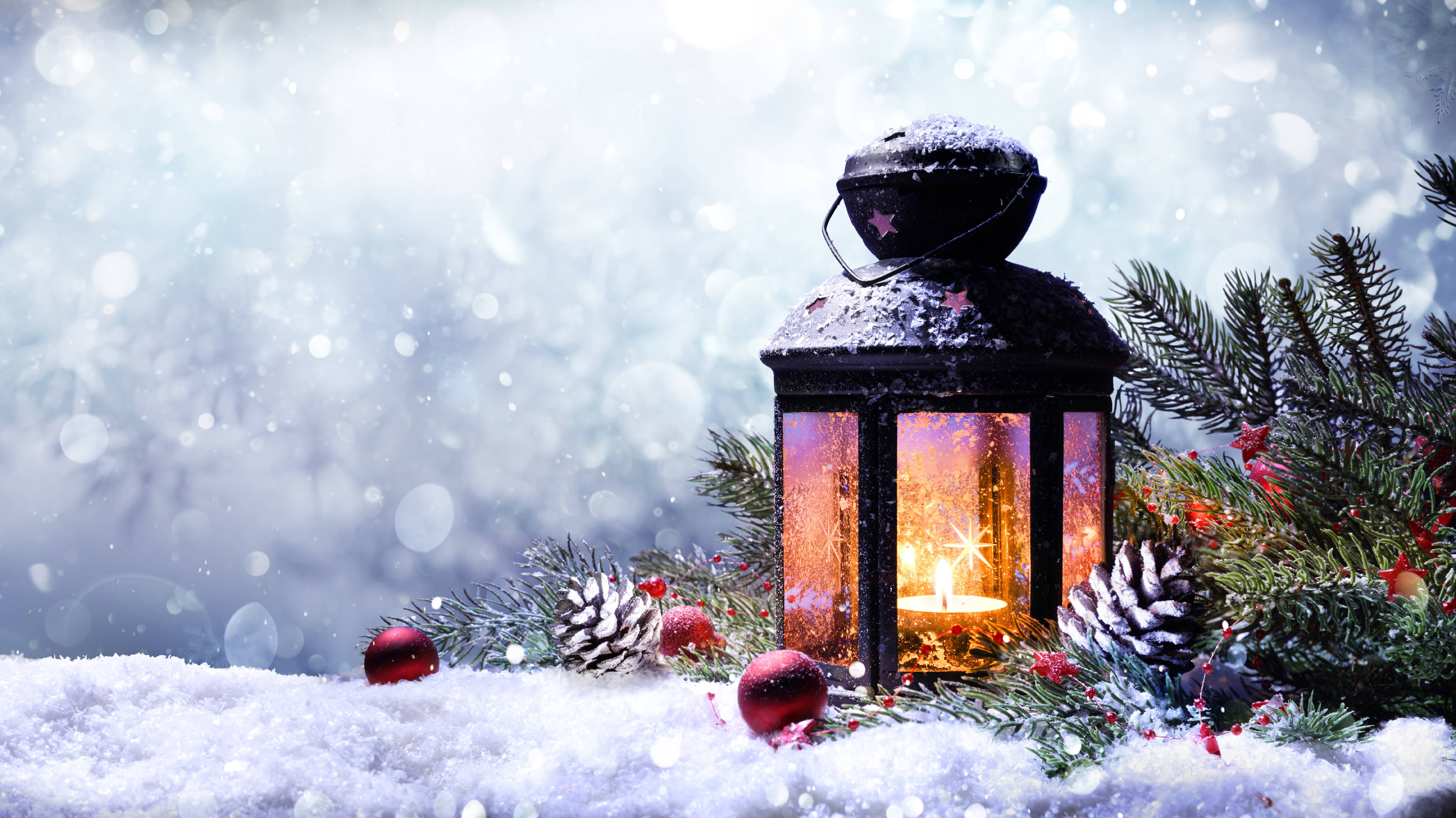 8K 聖誕節 桌布 壁紙 — 一盞發光的燈籠放在雪中，旁邊有松樹枝和紅色裝飾品，雪花飄落。