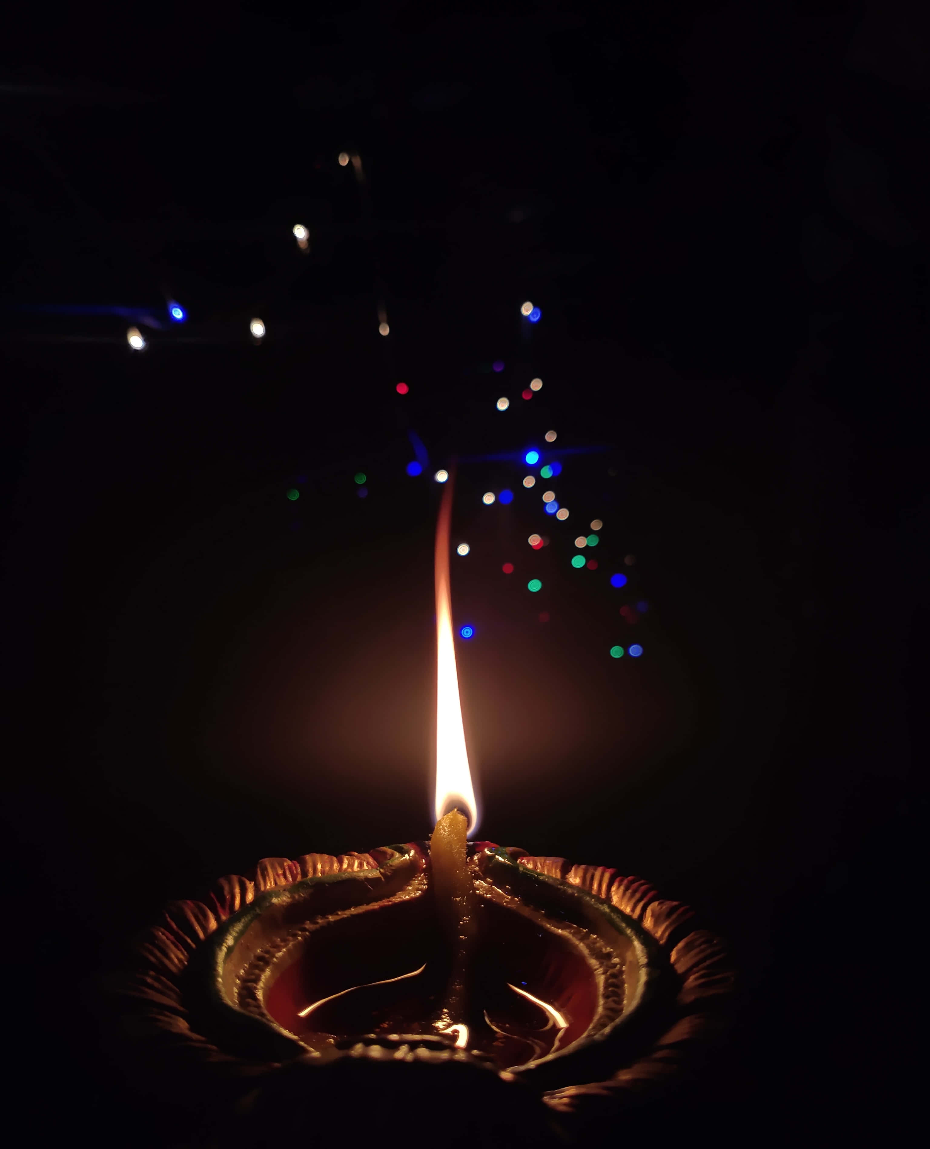 排燈節 桌布 壁紙 — 一盞發光的迪亞燈燭在點綴著彩色散景燈光的黑暗背景下溫暖地閃爍。