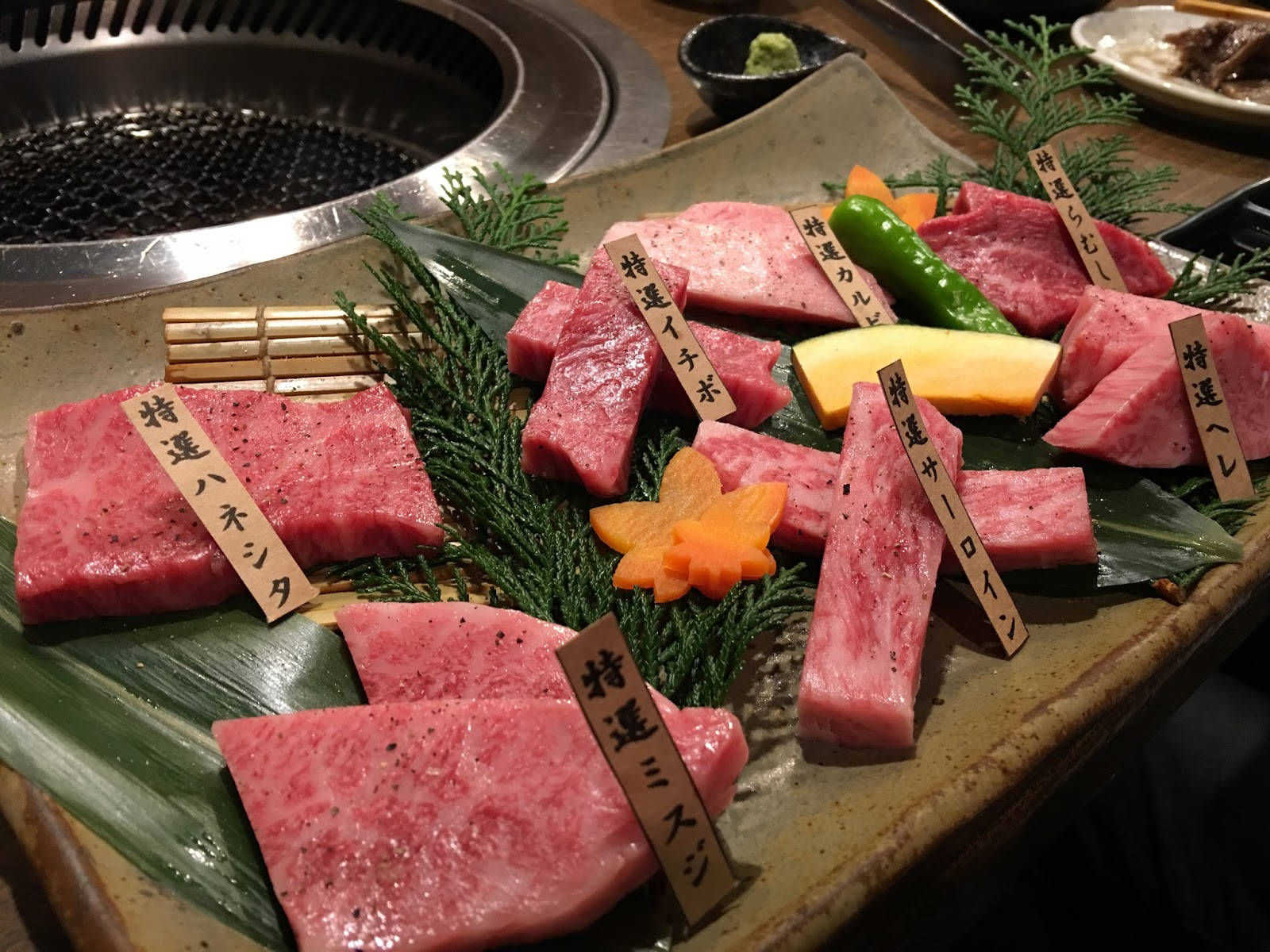 meat 桌布 壁紙 — 一盤優質日本和牛肉片，附有木牌和配菜，放在熱烤架旁。