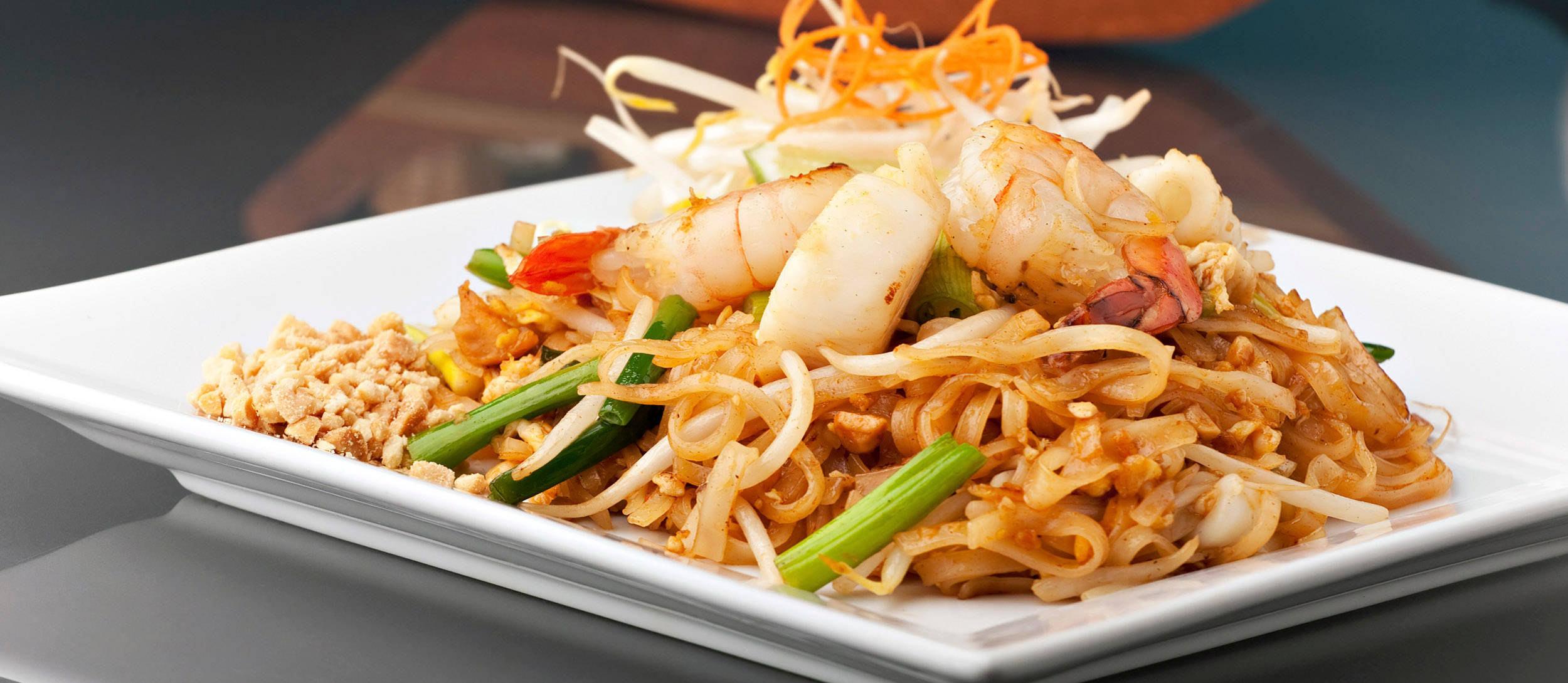 thai 桌布 壁紙 — 一盤充滿活力的泰式炒金邊粉，配上蝦仁、豆芽和青蔥，並以刨絲紅蘿蔔點綴。