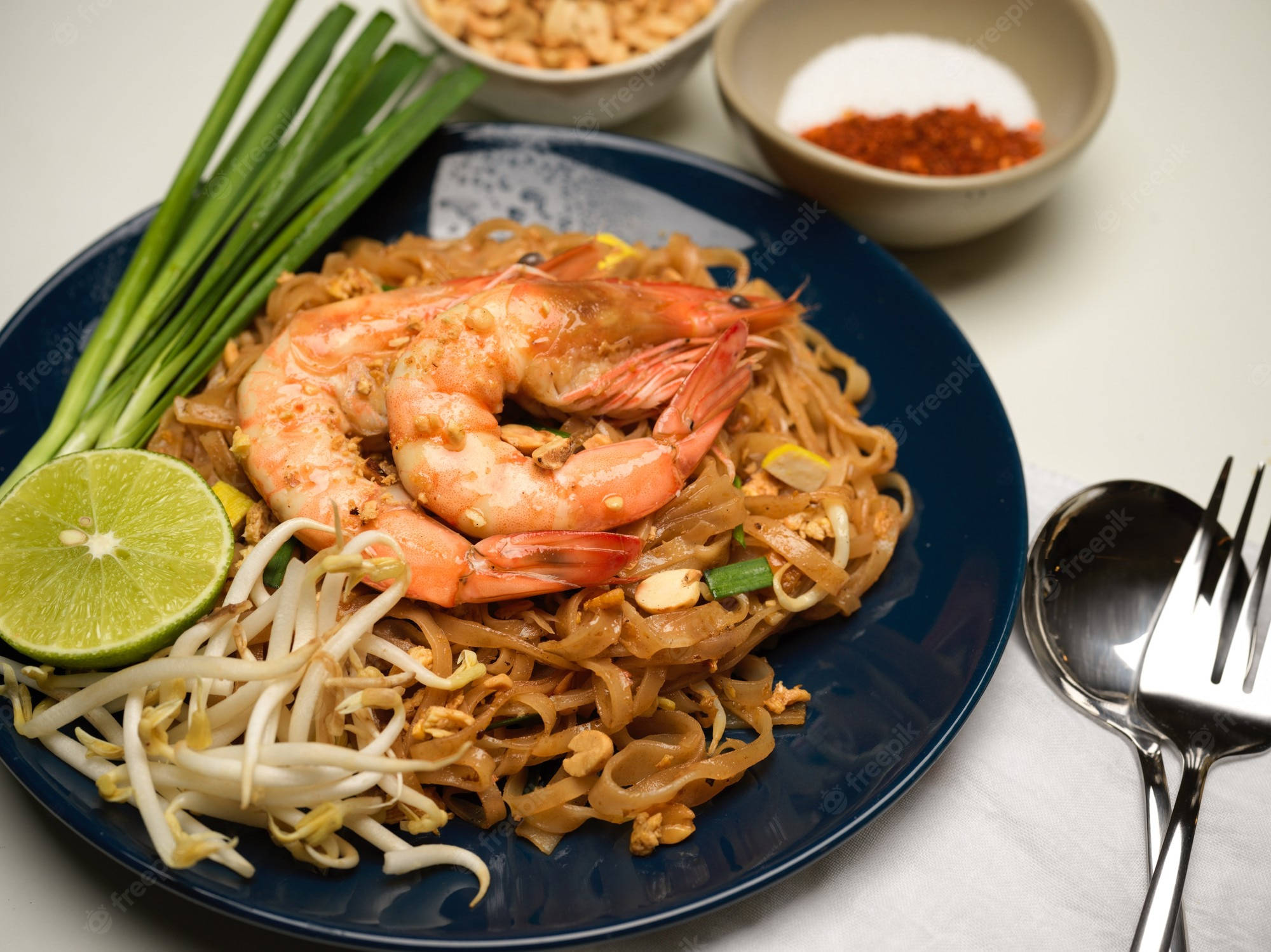 thai 桌布 壁紙 — 一盤充滿活力的泰式炒金邊粉，配上蝦、豆芽、青檸和辣椒裝飾，放在深藍色盤子上。