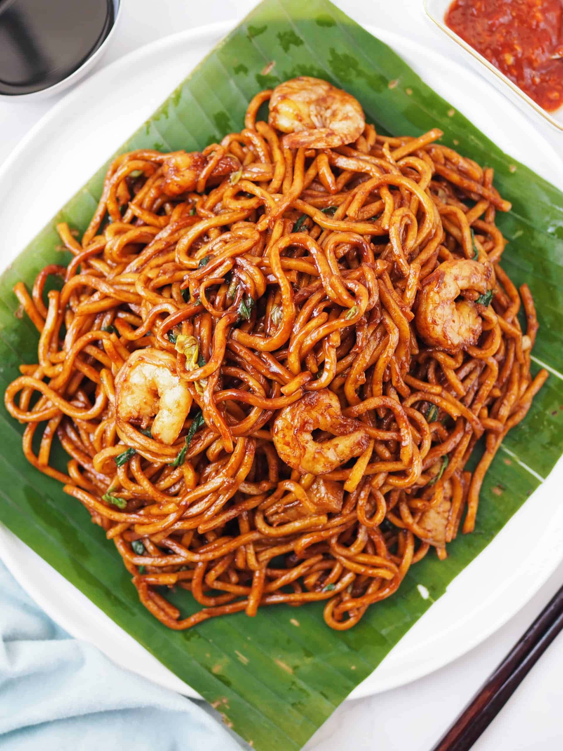 Delicious Food 桌布 壁紙 — 一盤光澤的棕色麵條配上蝦和香草，放在綠色香蕉葉上，附有蘸醬。